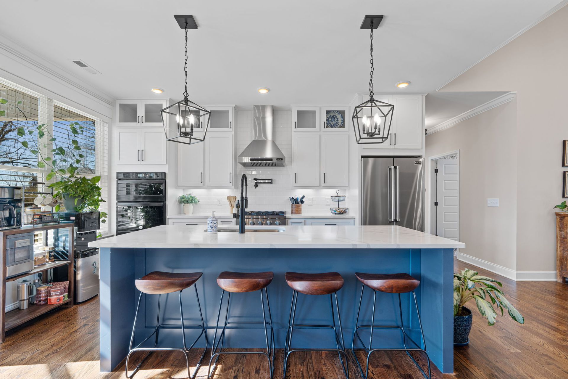 A kitchen with white cabinets and a blue island with stools.