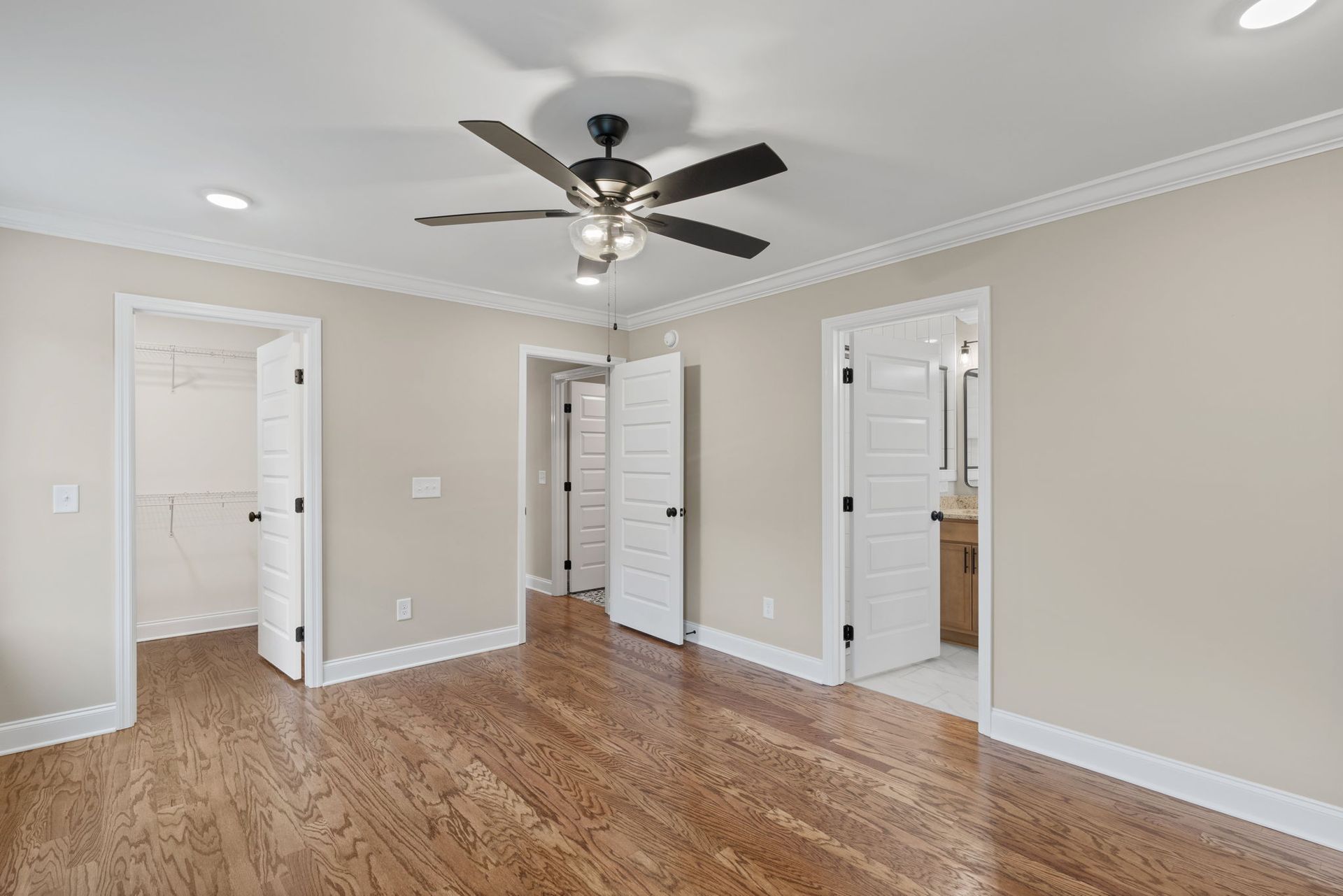 An empty bedroom with hardwood floors and a ceiling fan.