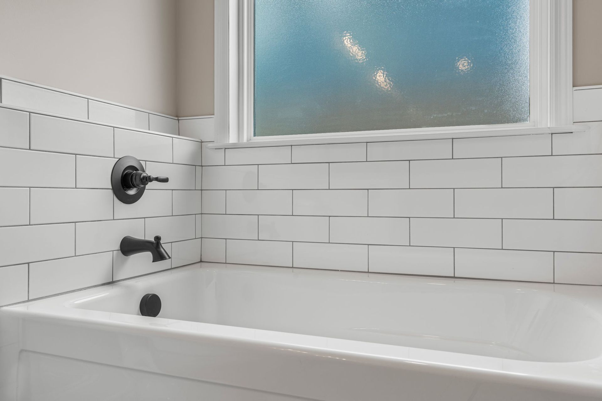 A bathtub in a bathroom with white tiles and a window.