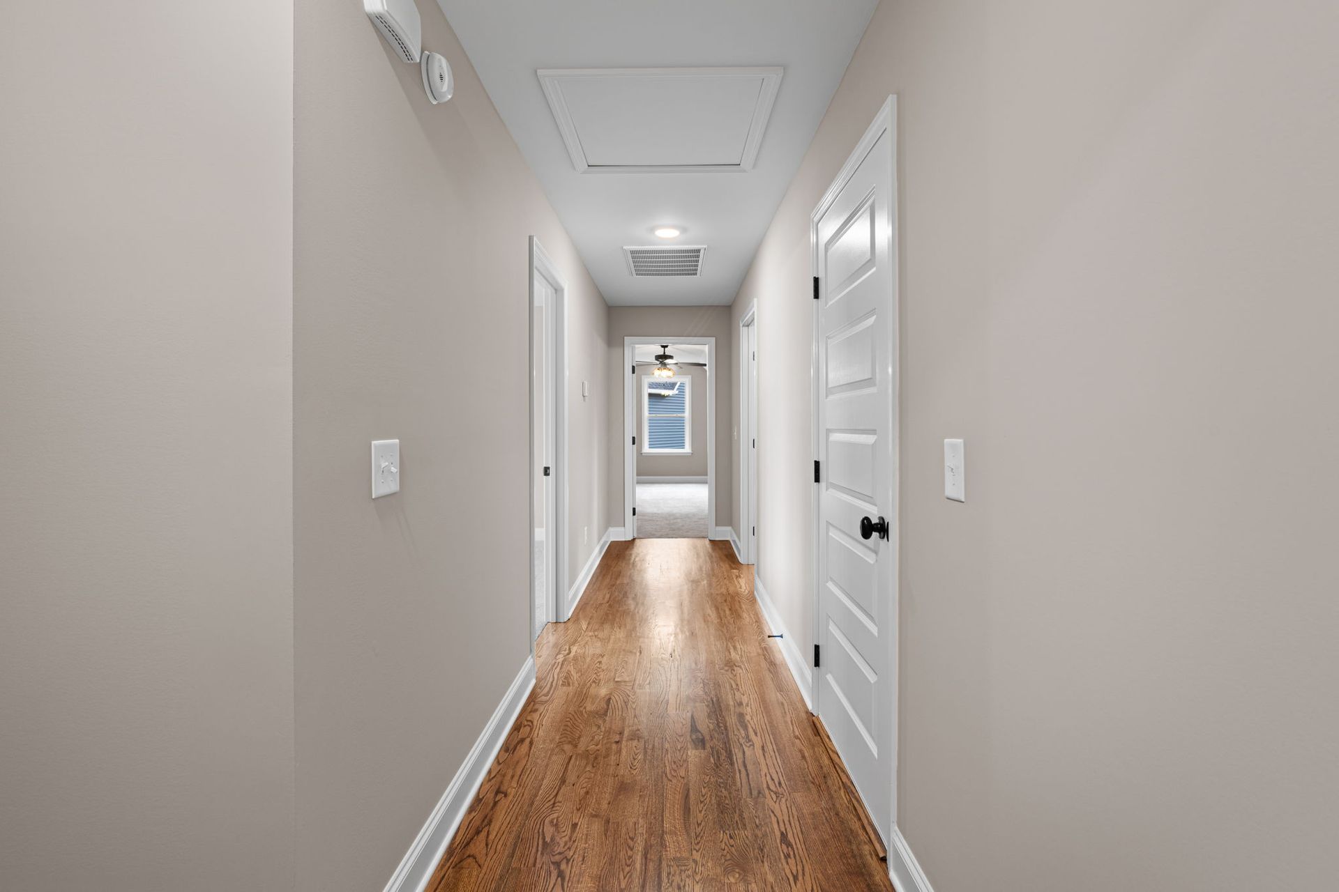 A long hallway with hardwood floors and white doors in a house.
