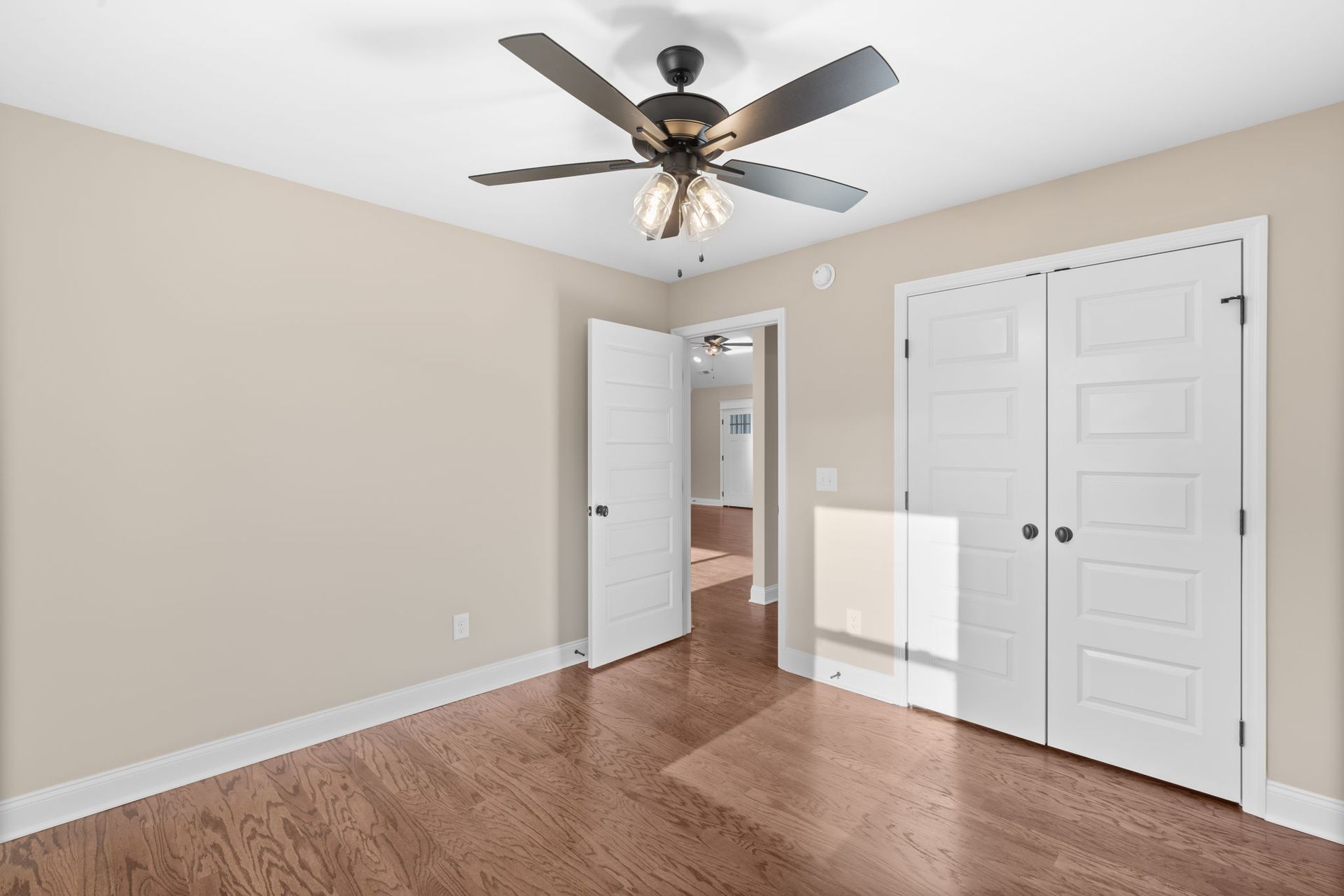An empty bedroom with hardwood floors and a ceiling fan.