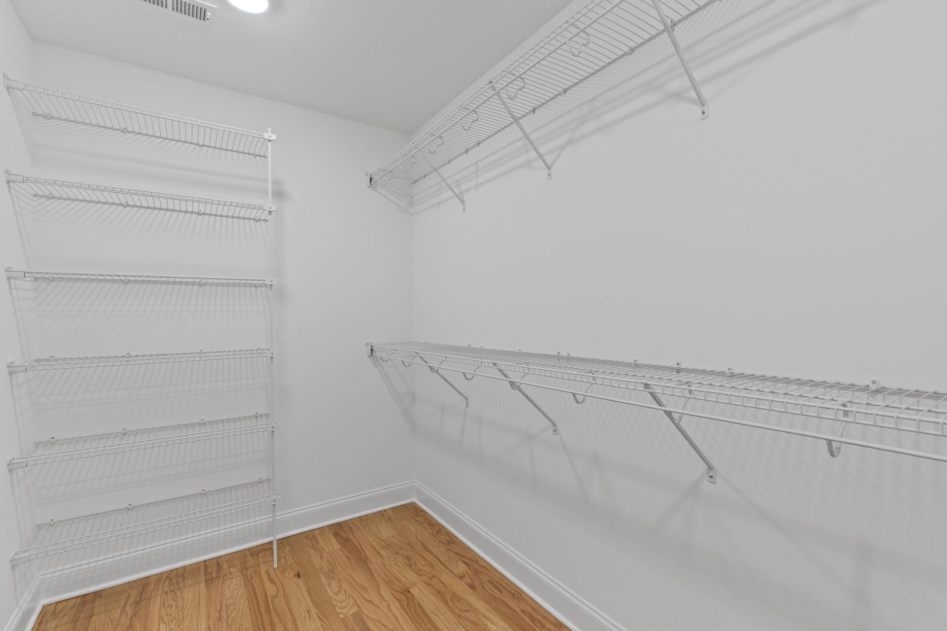 A walk in closet with lots of shelves and a wooden floor.
