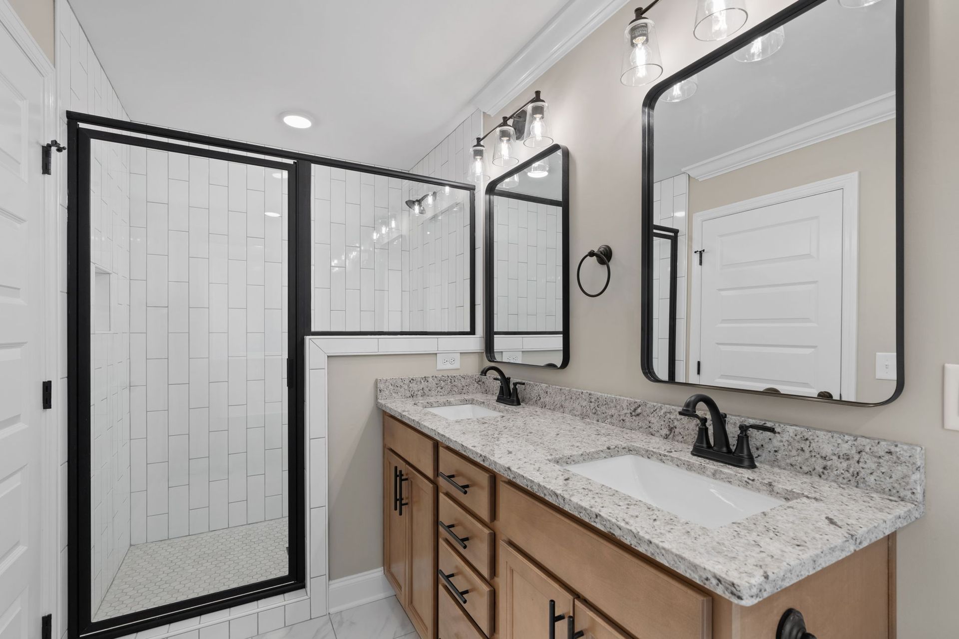 A bathroom with two sinks , two mirrors and a walk in shower.