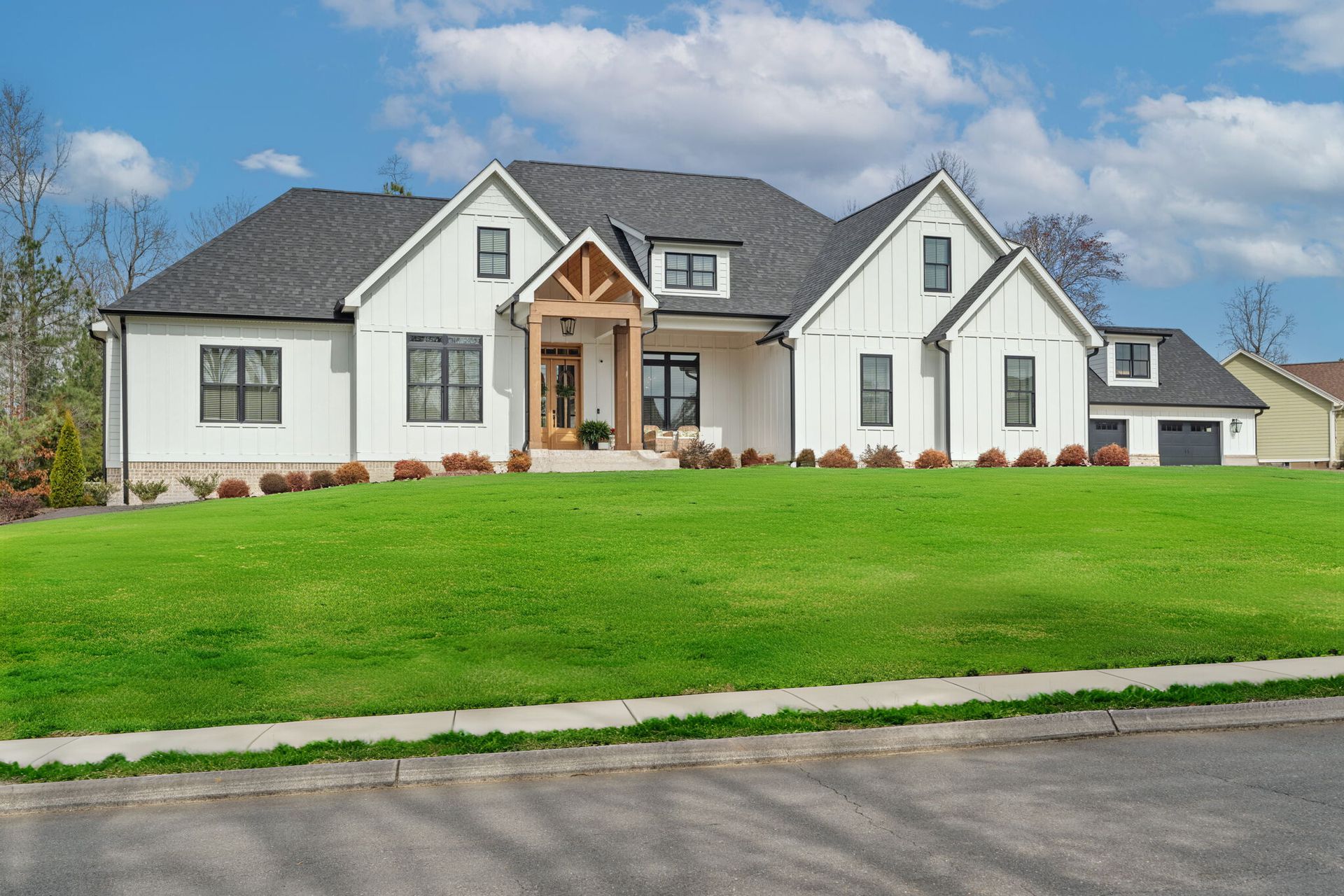 A large white house with a gray roof is sitting on top of a lush green hill.