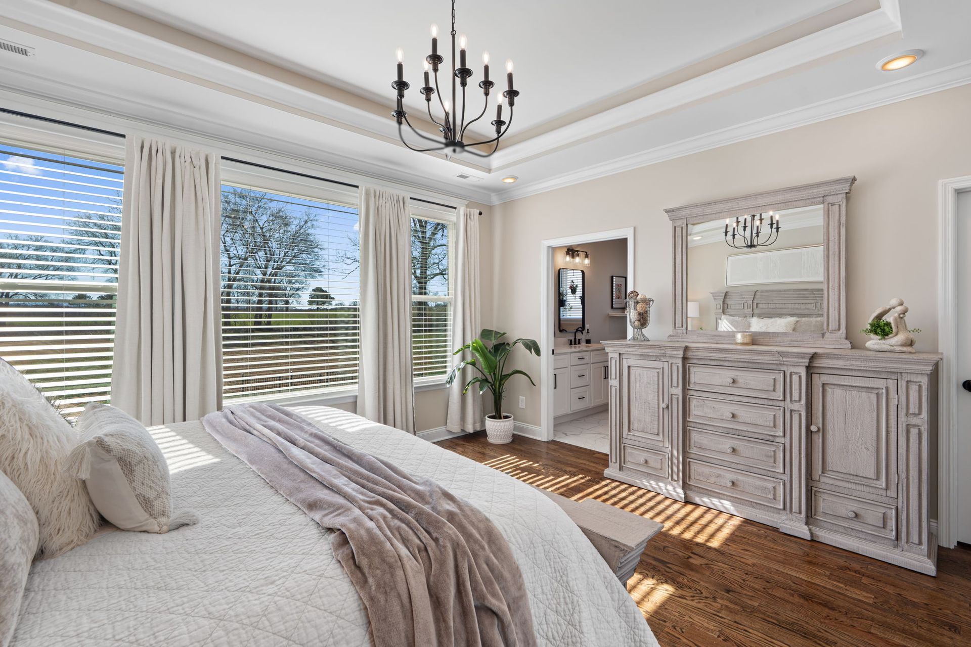 A bedroom with a bed , dresser , mirror and chandelier.