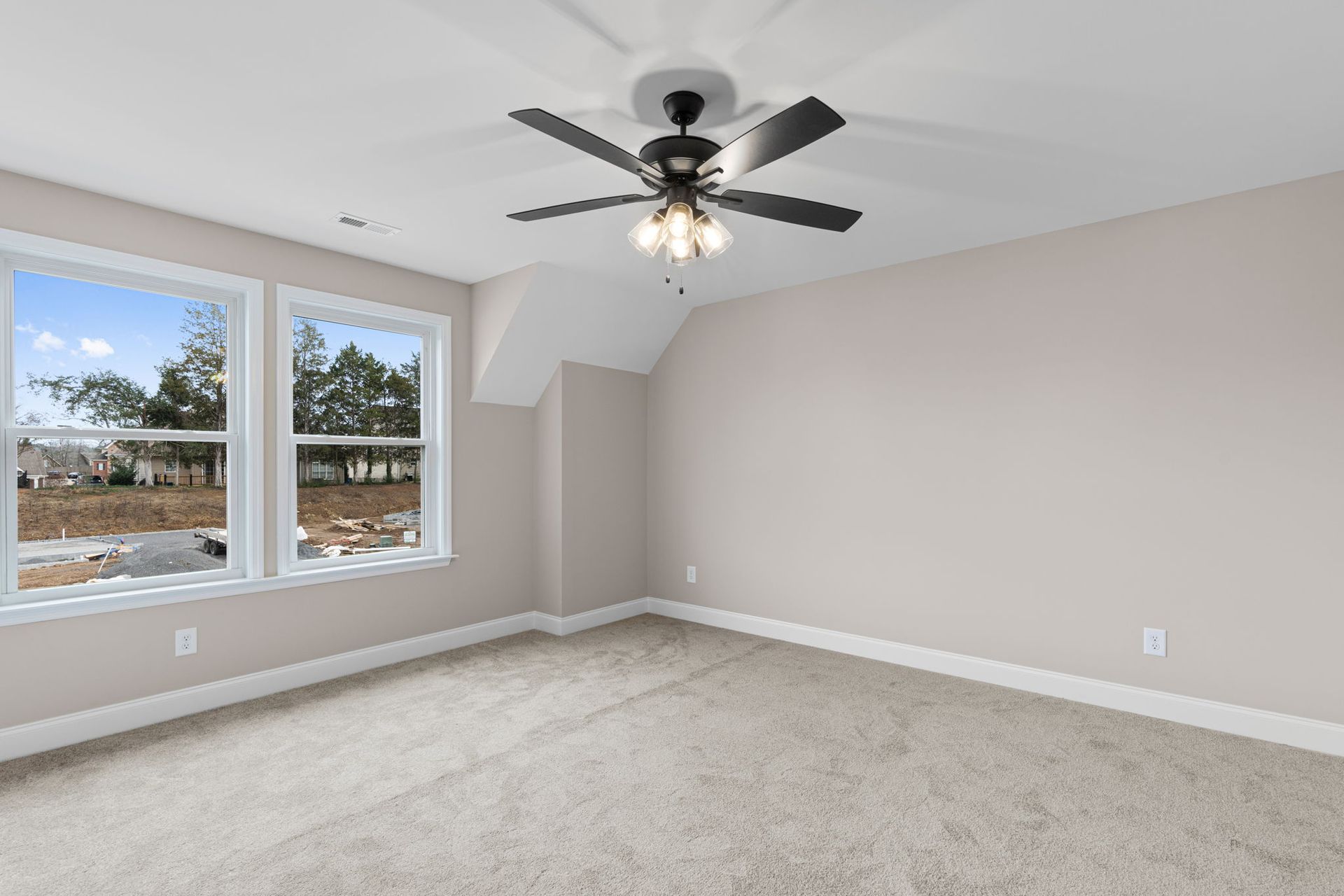 An empty bedroom with a ceiling fan and two windows.