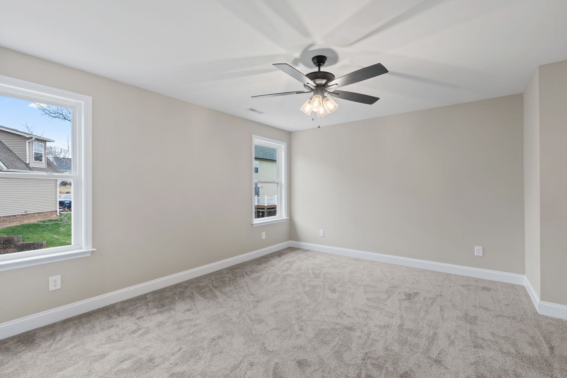 An empty bedroom with a ceiling fan and two windows.