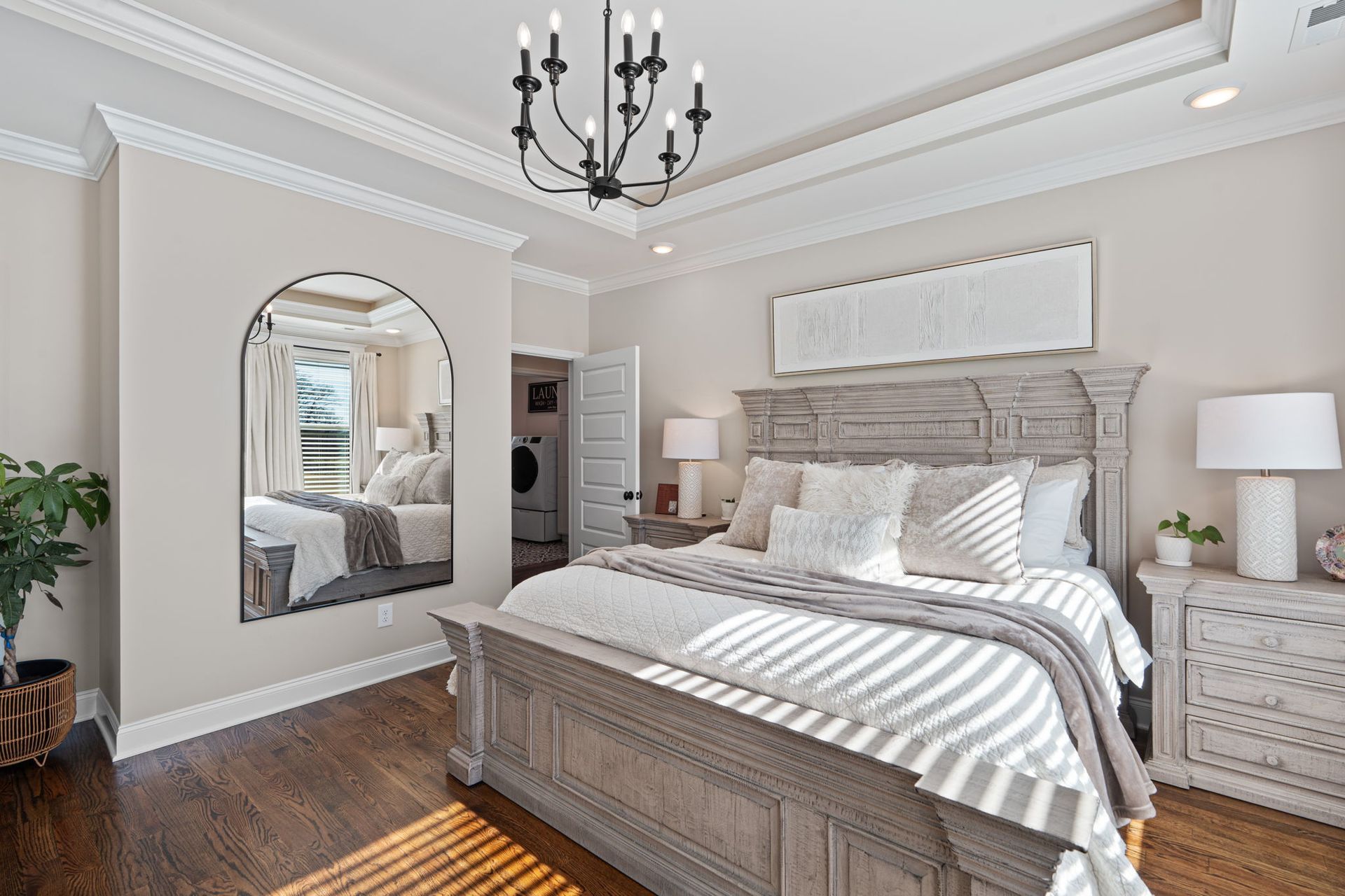 A bedroom with a bed , dresser , nightstand , mirror and chandelier.