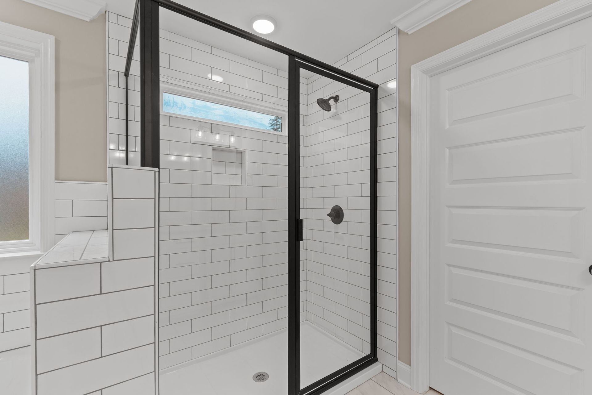 A bathroom with white tiles and a walk in shower with a black frame.