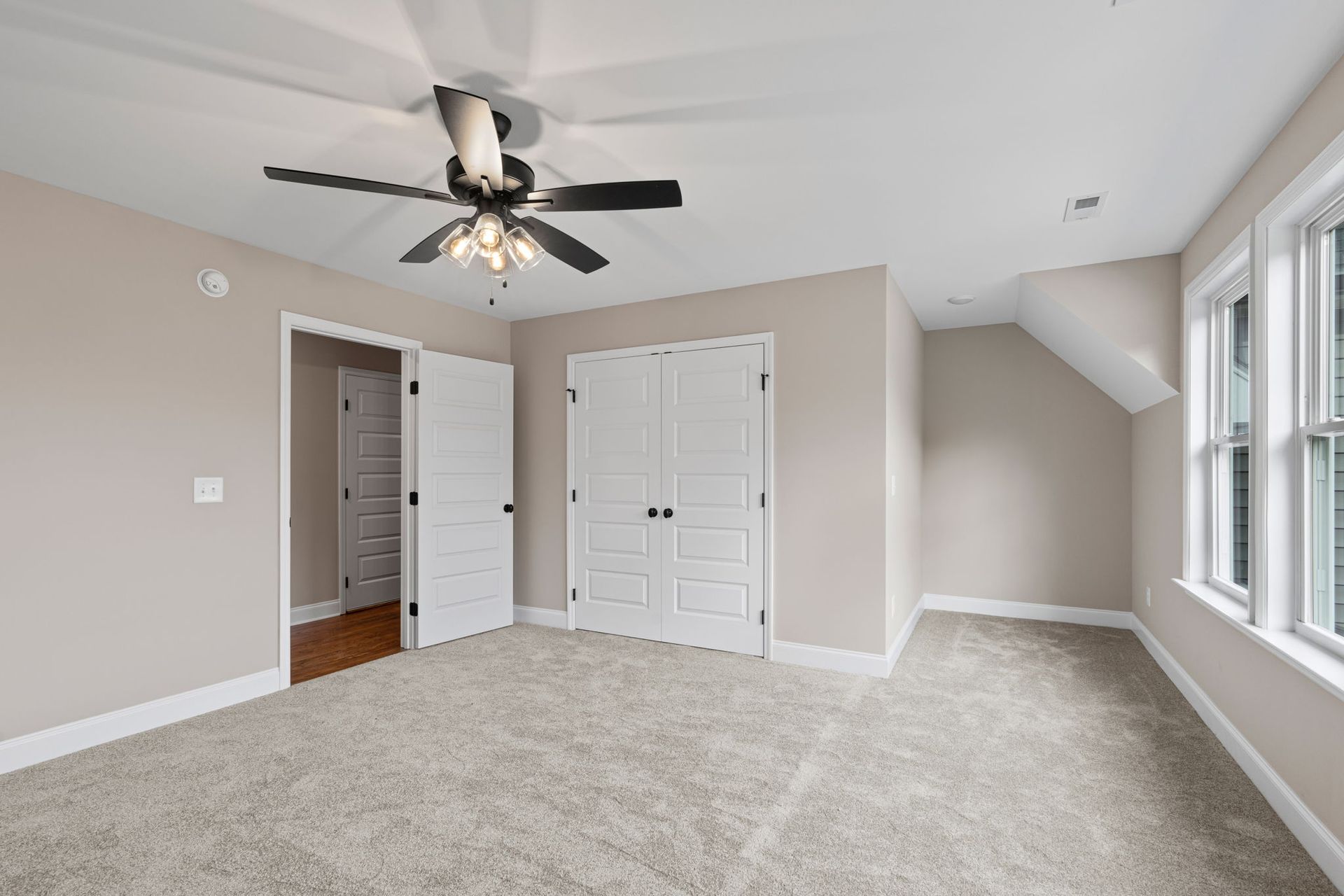 An empty bedroom with a ceiling fan and two windows.