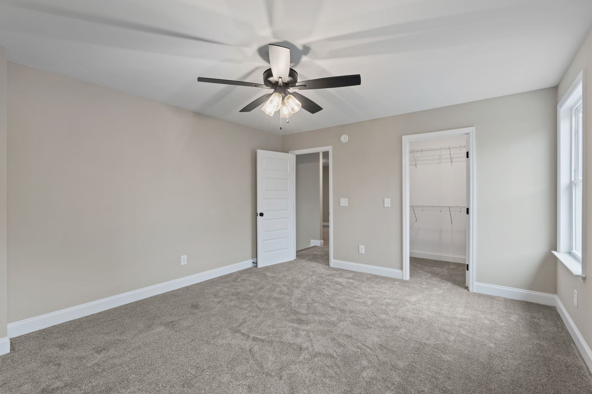 An empty bedroom with a ceiling fan and a window.