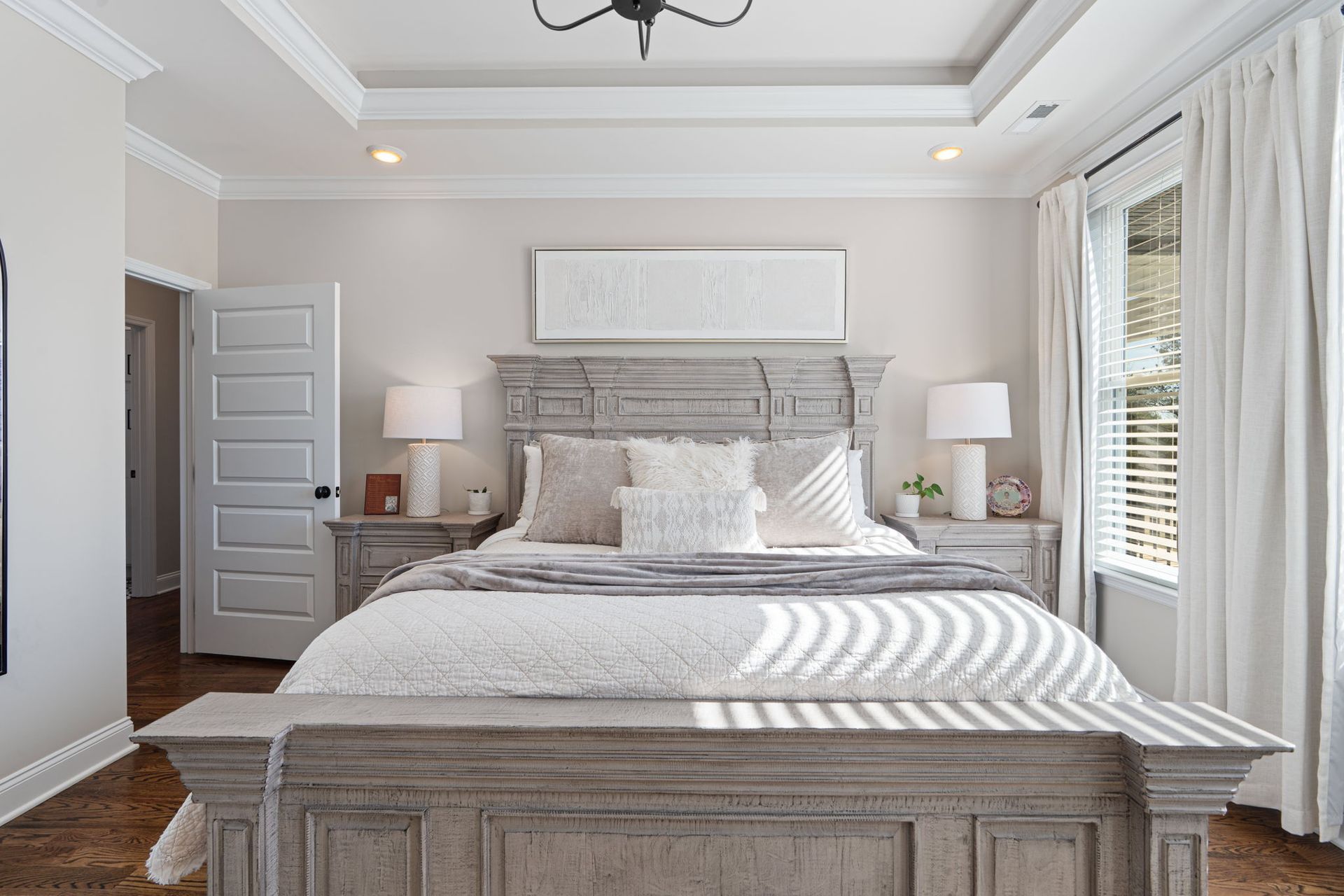 A bedroom with a king size bed , nightstands , lamps and a window.