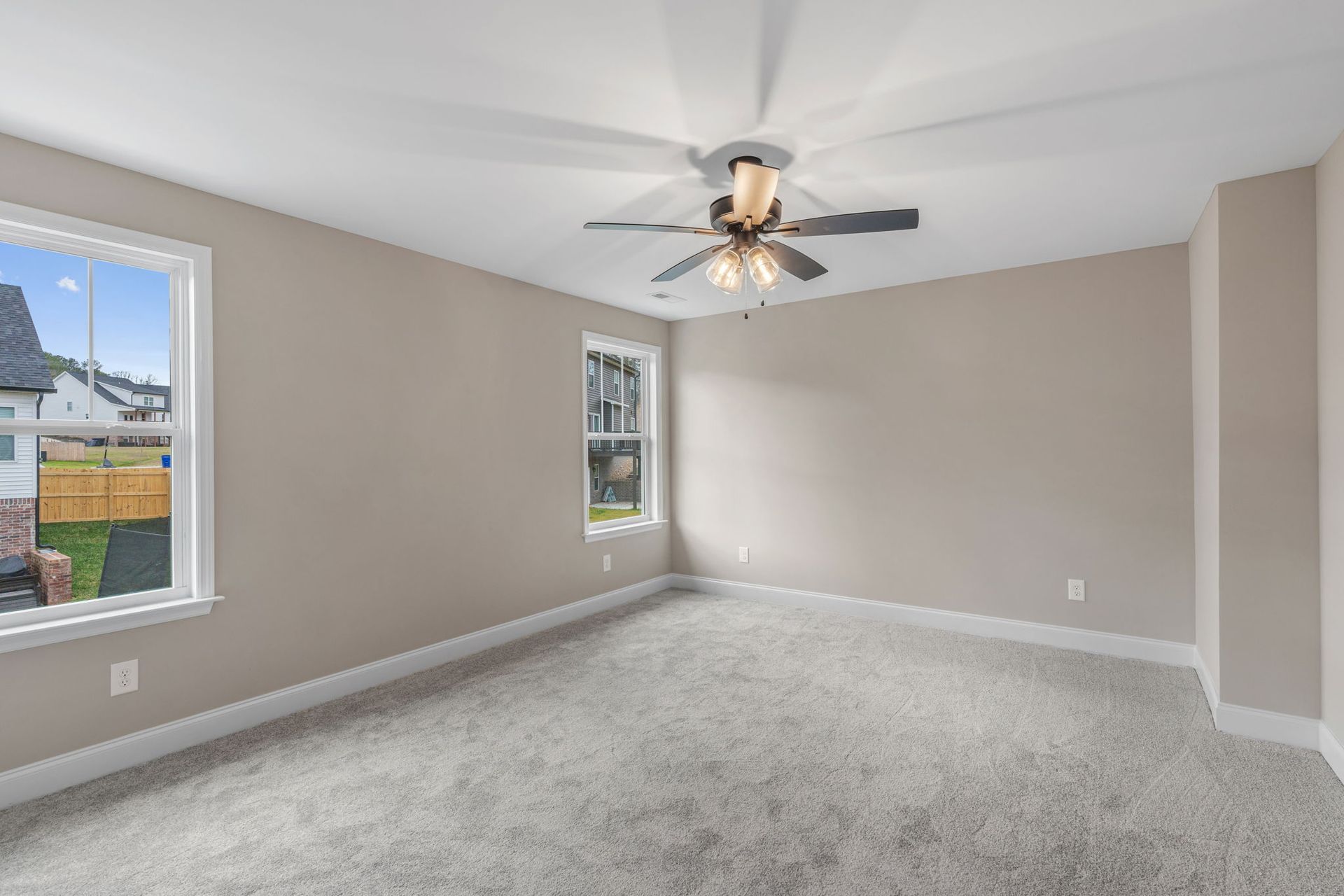 An empty bedroom with a ceiling fan and two windows.