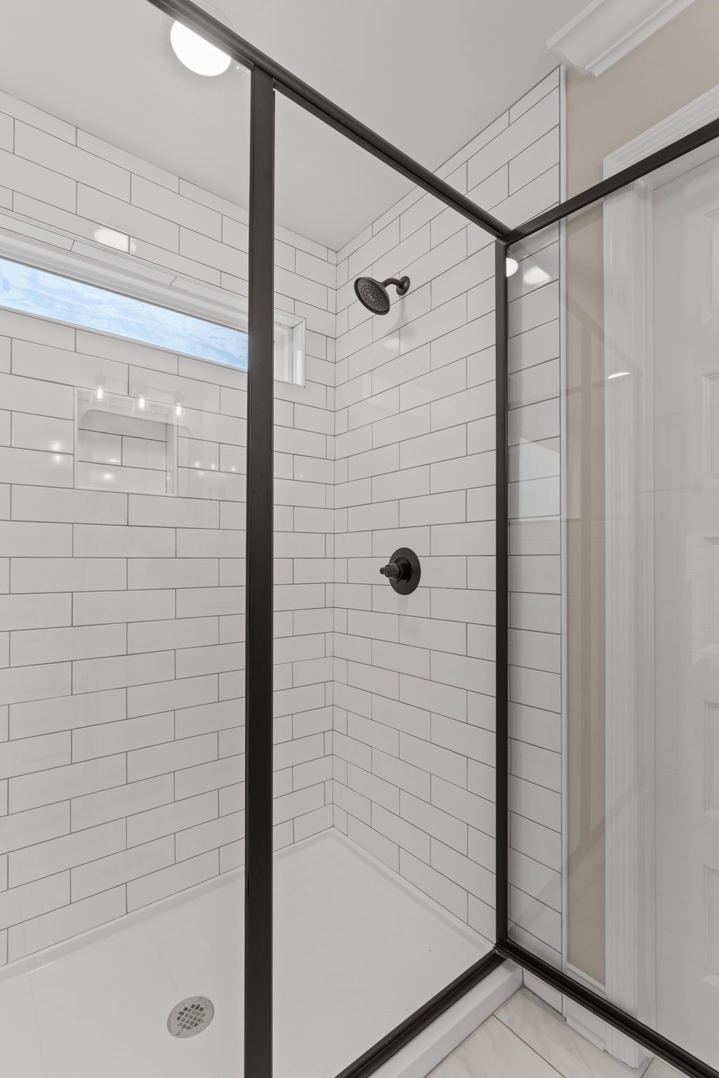 A bathroom with white subway tiles and a walk in shower with a black frame.