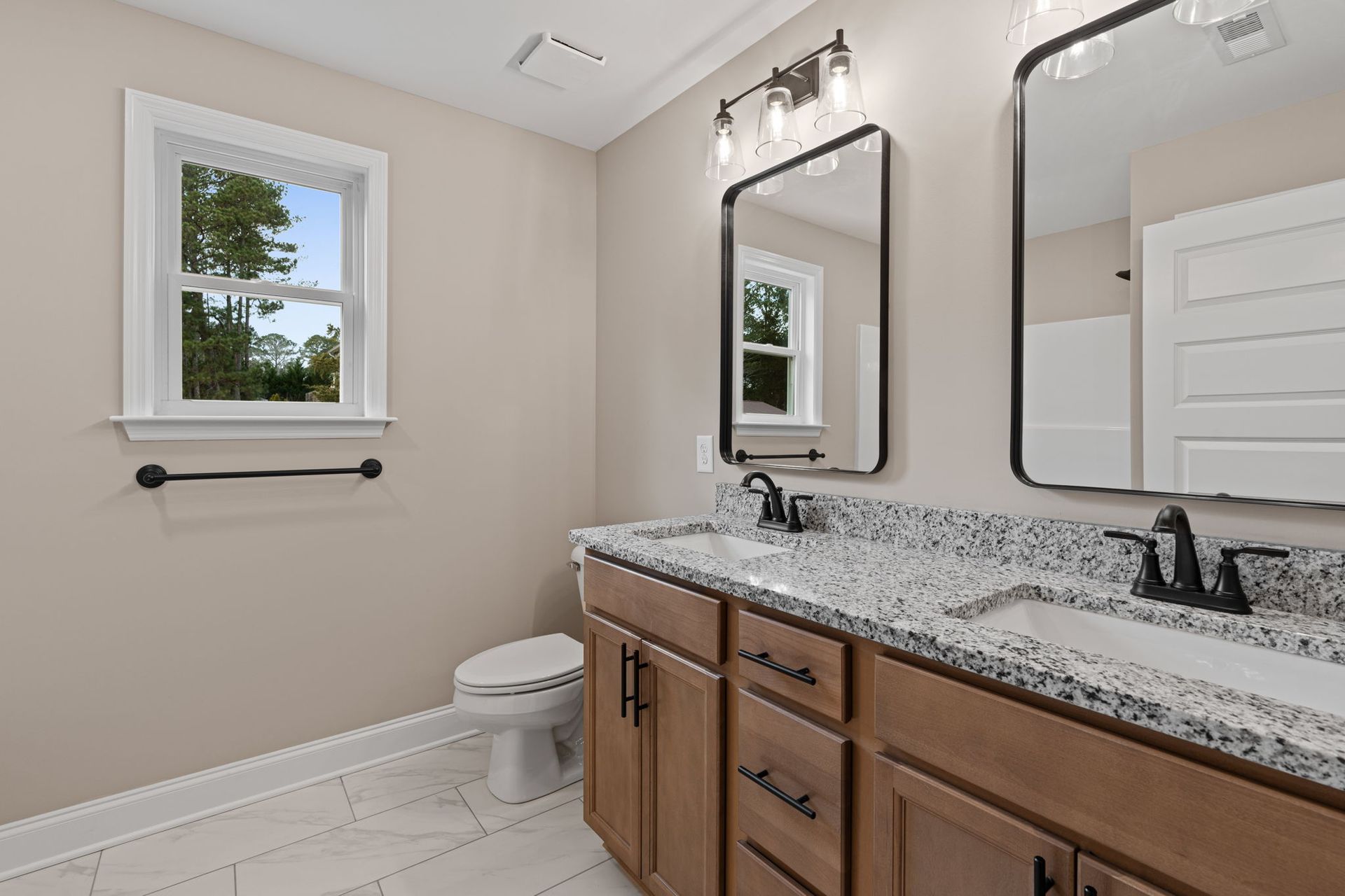 A bathroom with two sinks , a toilet , and two mirrors.