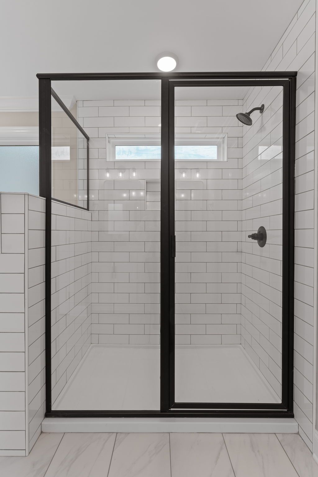 A bathroom with white tiles and a black shower door.