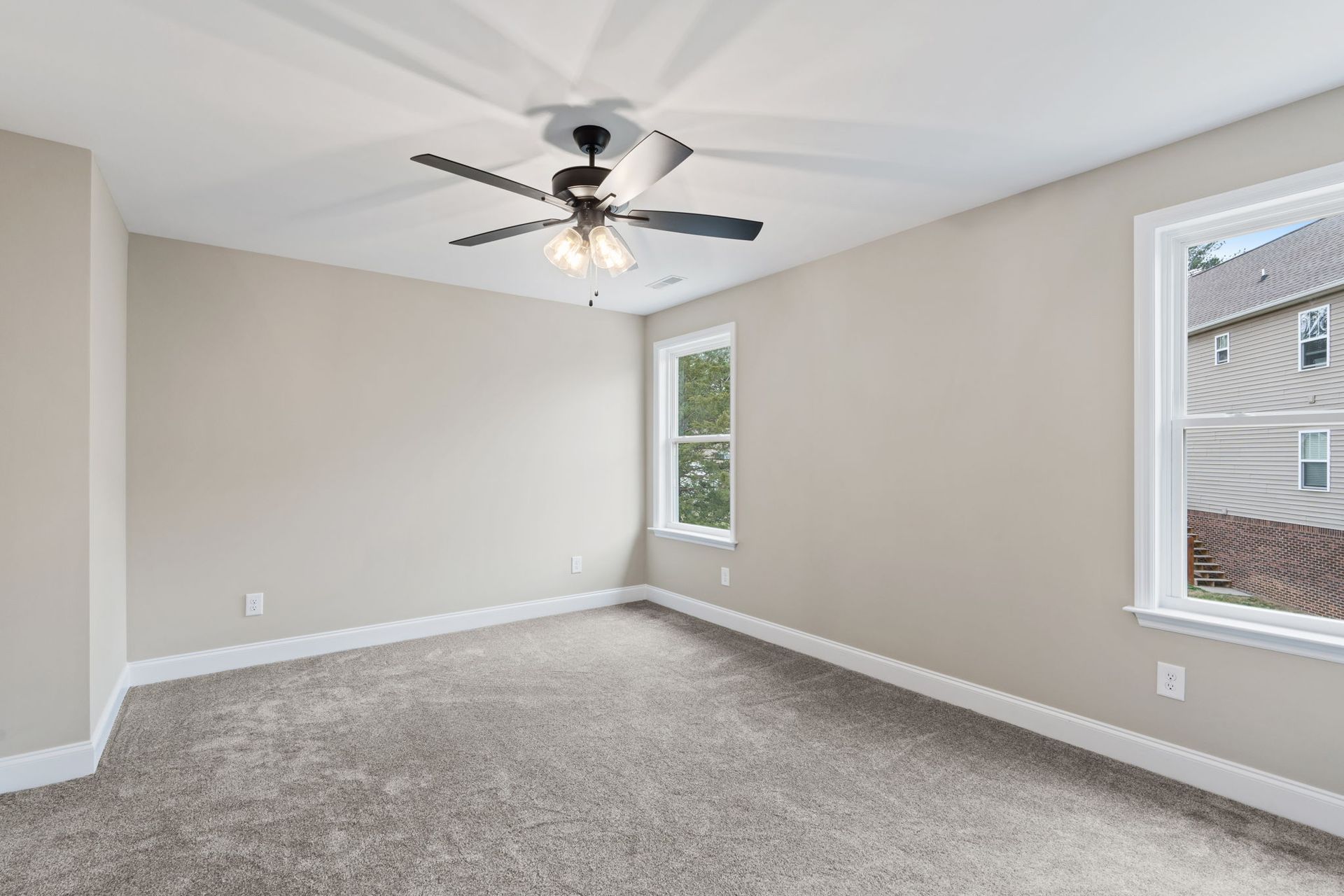 An empty bedroom with a ceiling fan and two windows.