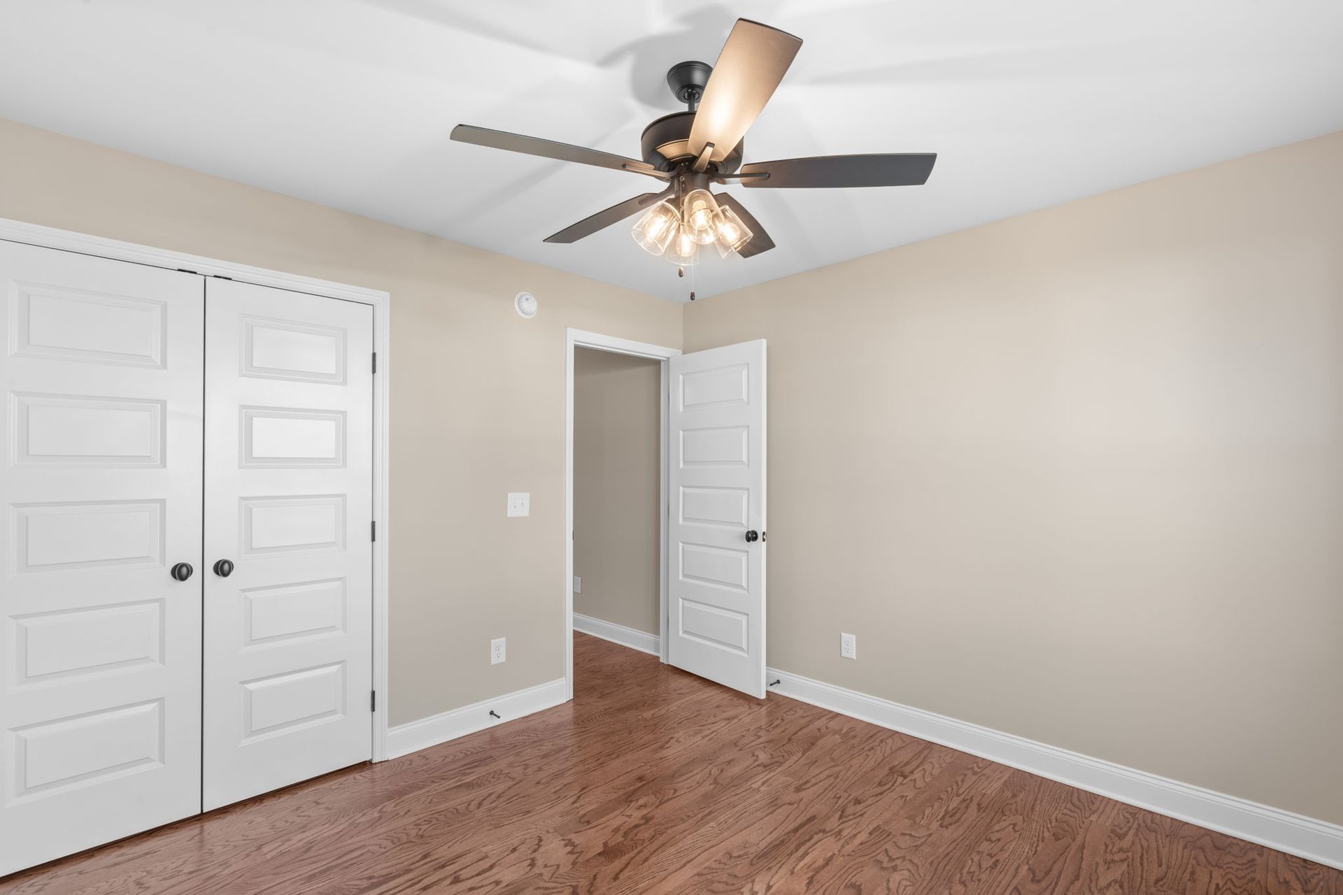An empty bedroom with hardwood floors and a ceiling fan.