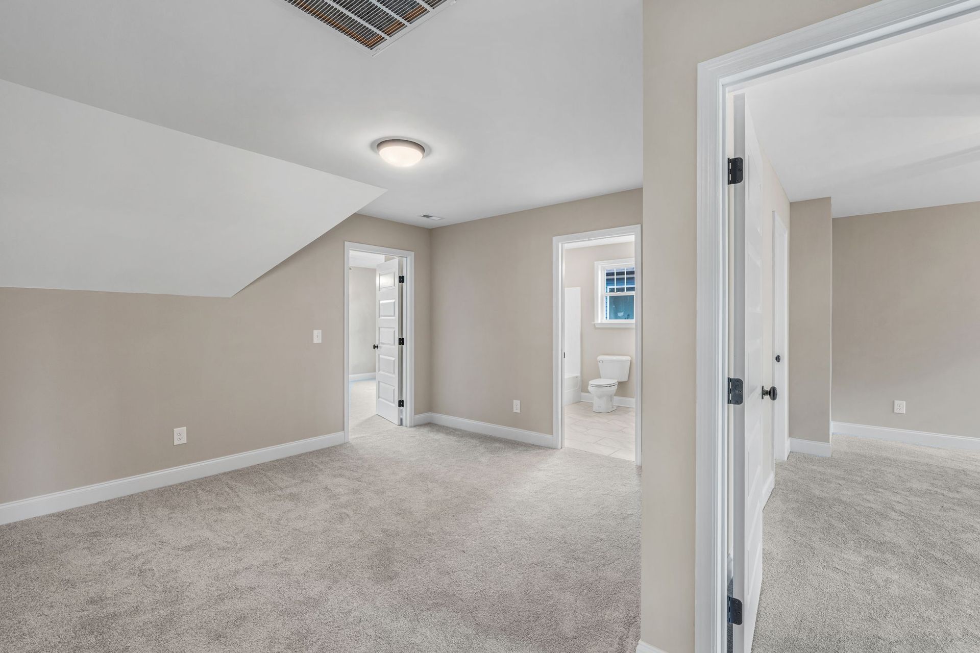 An empty room with a carpeted floor and a ceiling fan in a house.