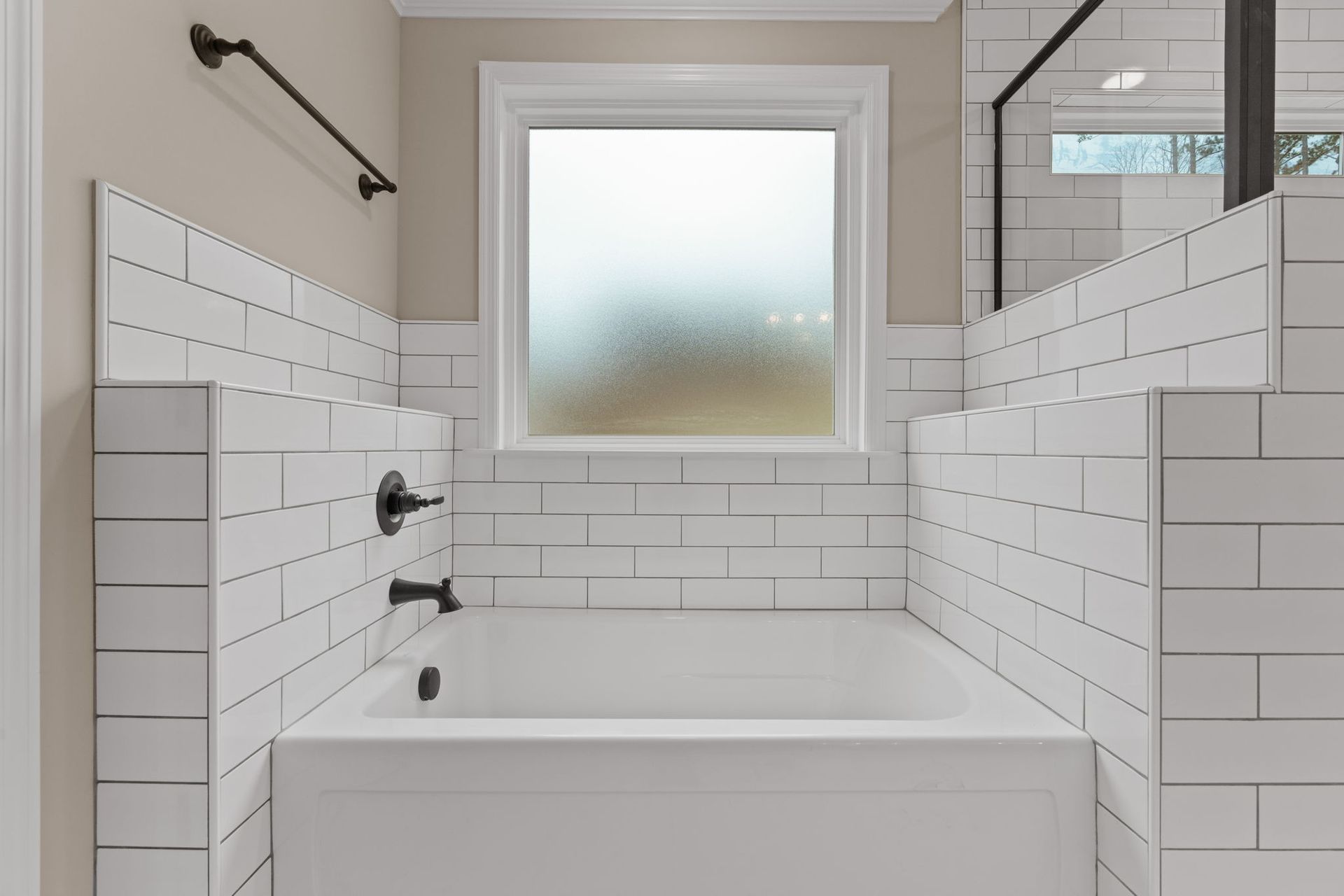 There is a bathtub in the bathroom with white tiles and a window.