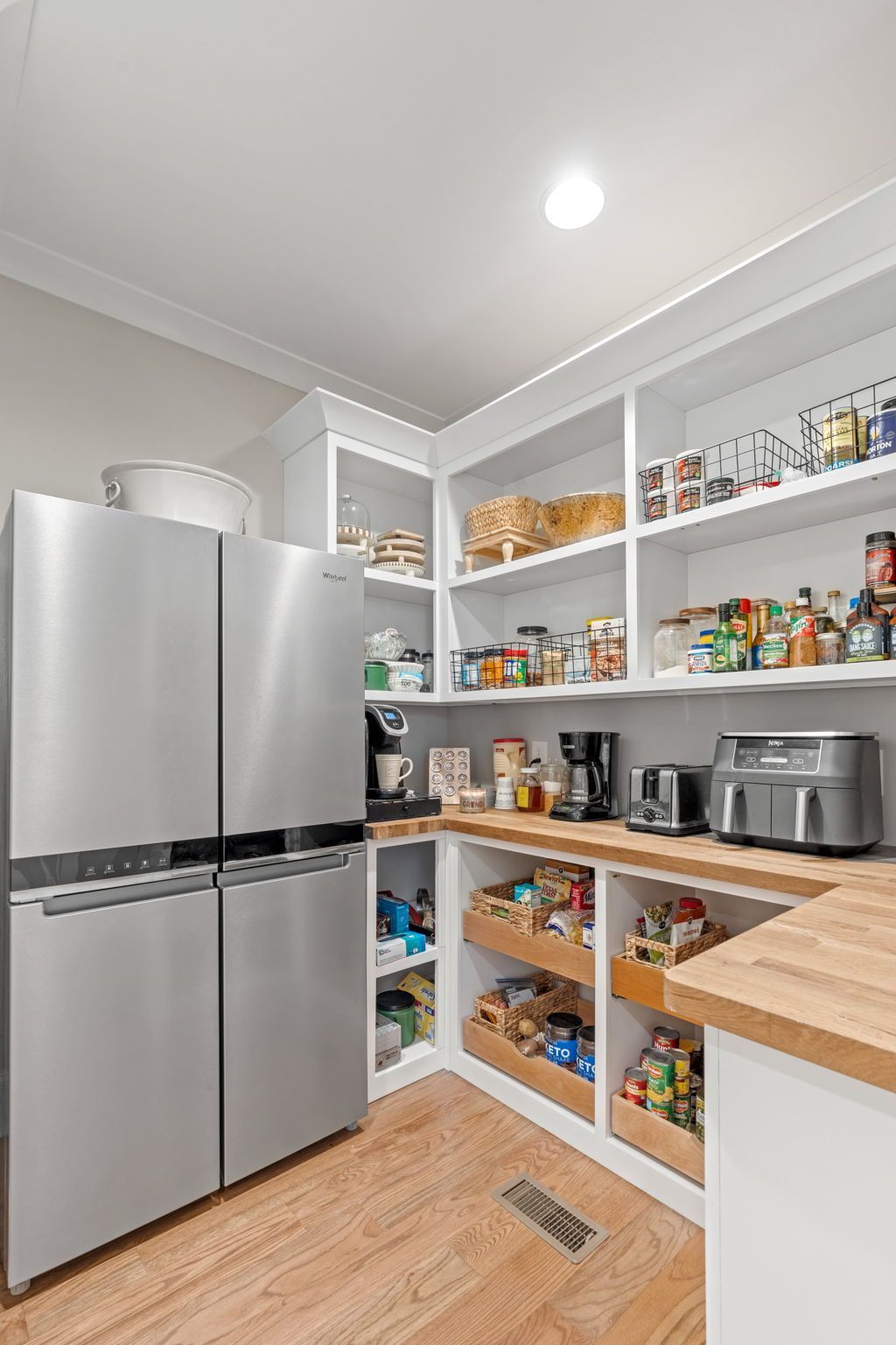 A kitchen with a stainless steel refrigerator and a pantry filled with food.