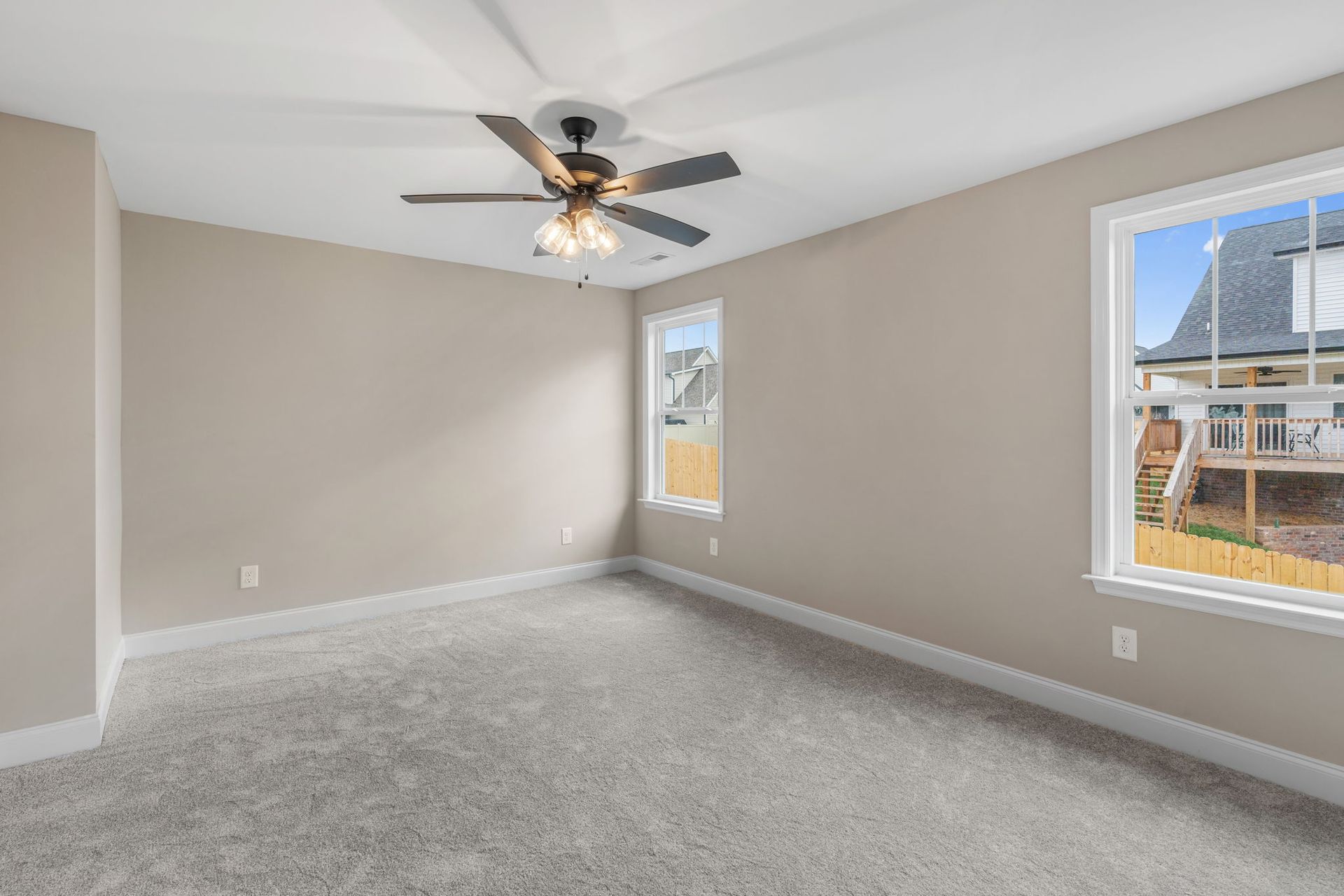 An empty bedroom with a ceiling fan and two windows.