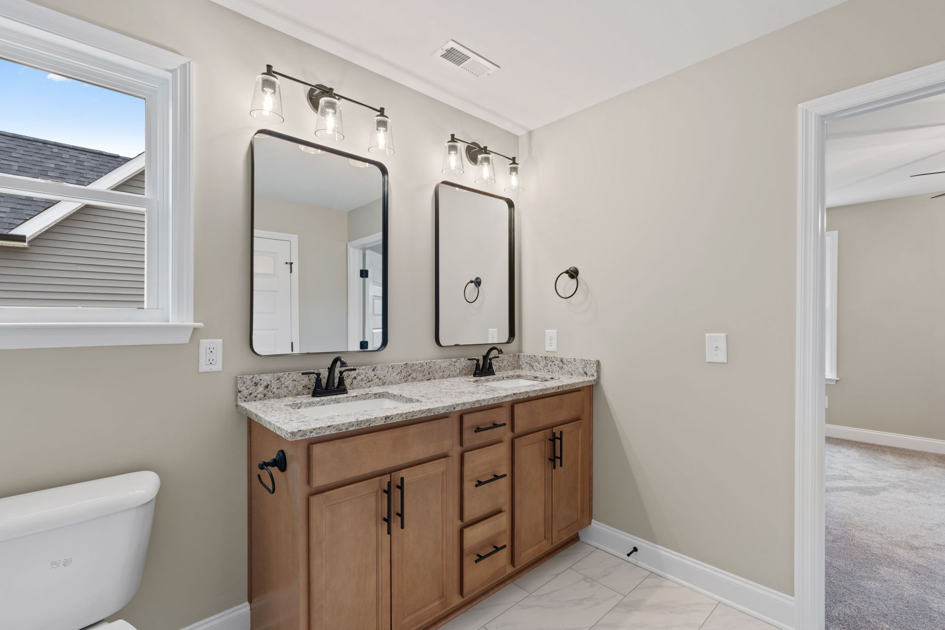 A bathroom with two sinks , two mirrors and a toilet.