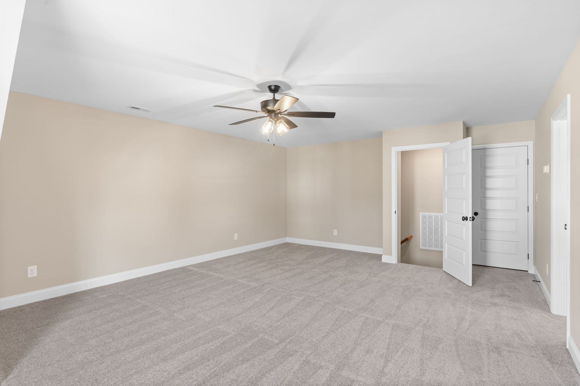 A large empty room with a ceiling fan and a staircase.