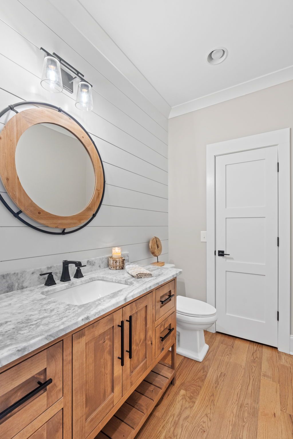 A bathroom with a sink , toilet , mirror and wooden cabinets.
