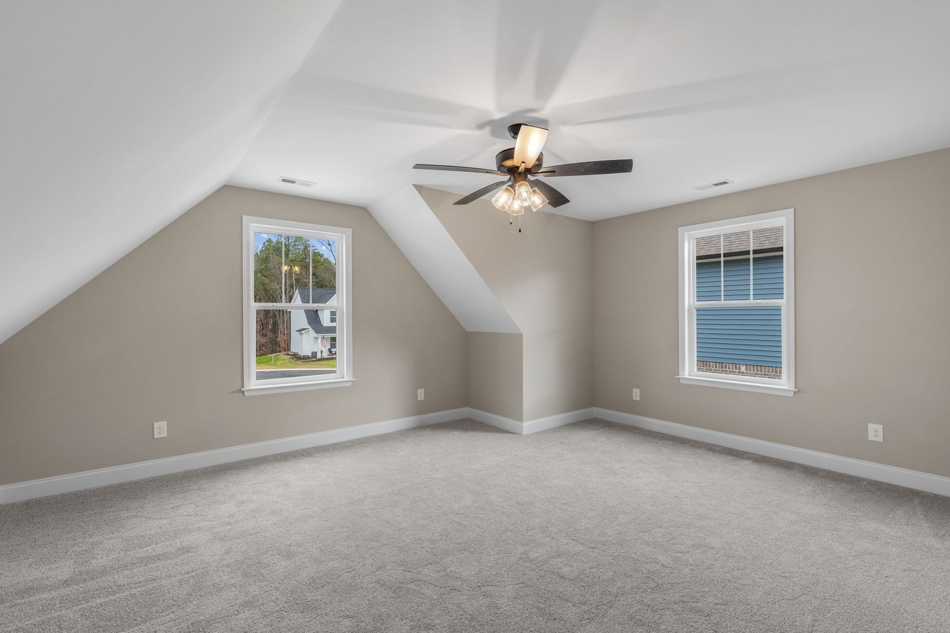 An empty bedroom with a ceiling fan and two windows.