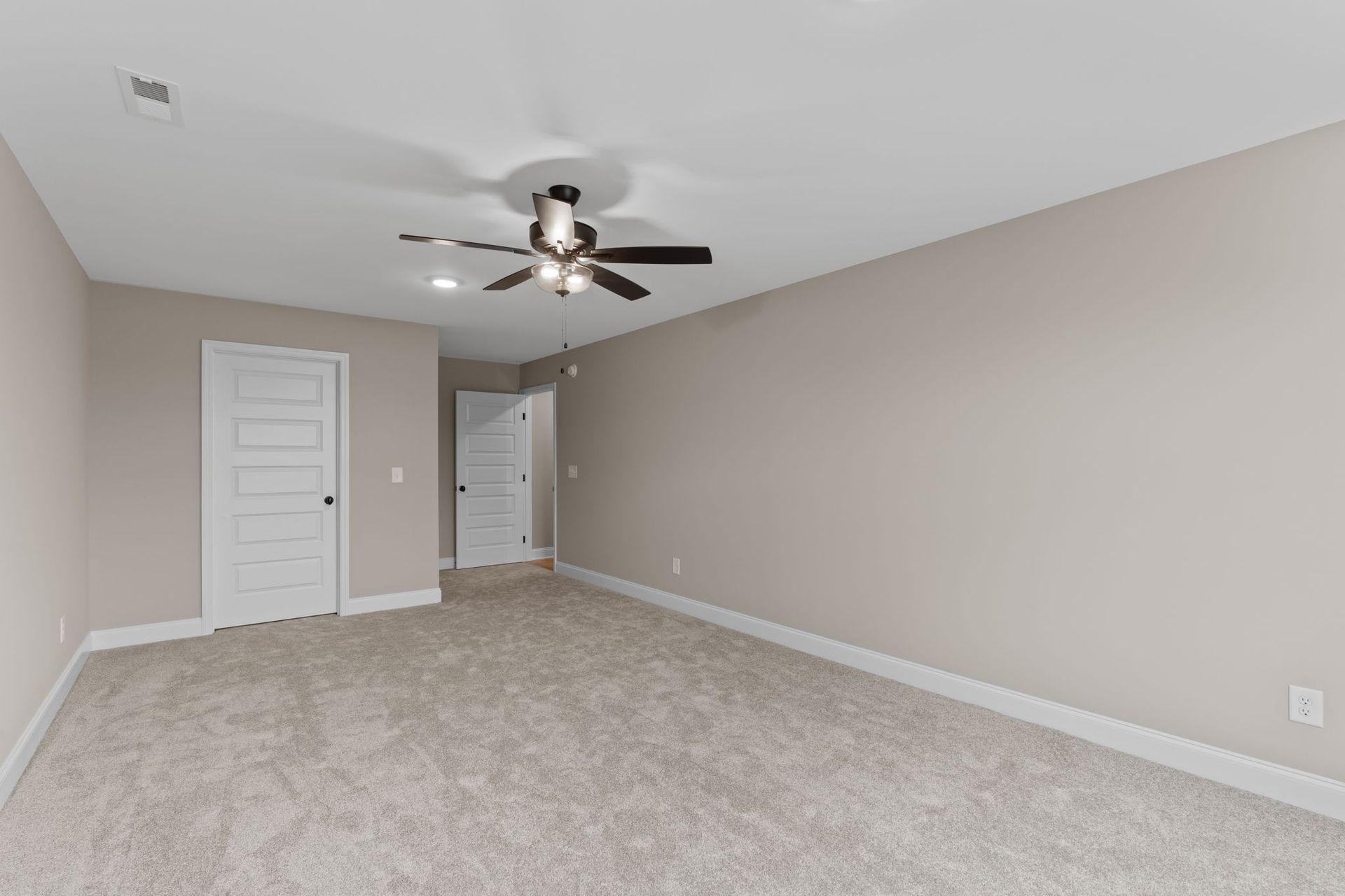 An empty bedroom with a ceiling fan and a carpeted floor.