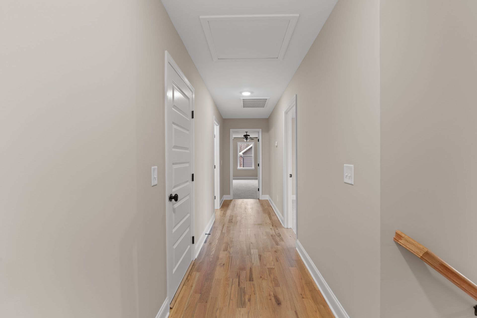 A long hallway with hardwood floors and stairs in a house.
