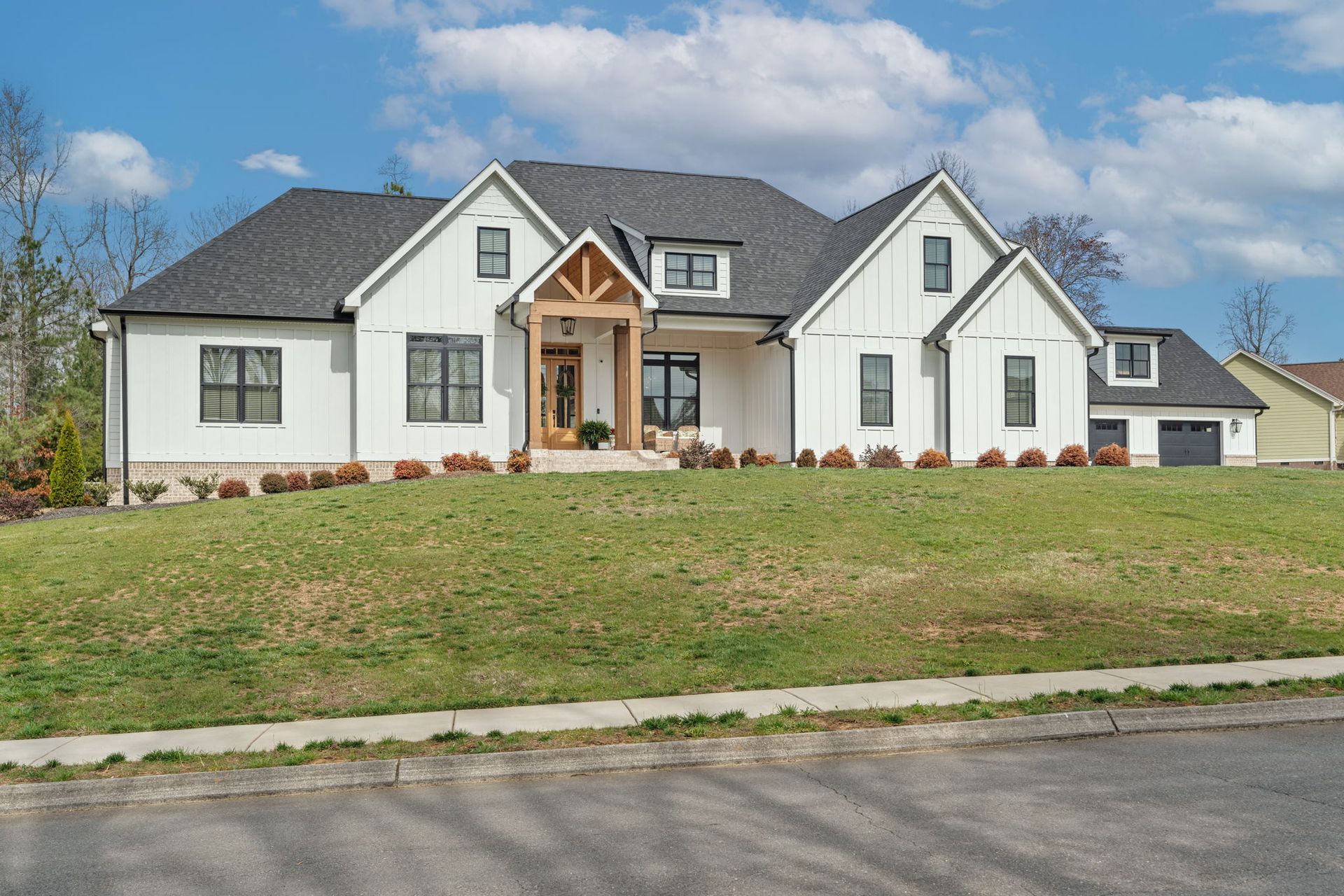 A large white house with a gray roof is sitting on top of a lush green hill.