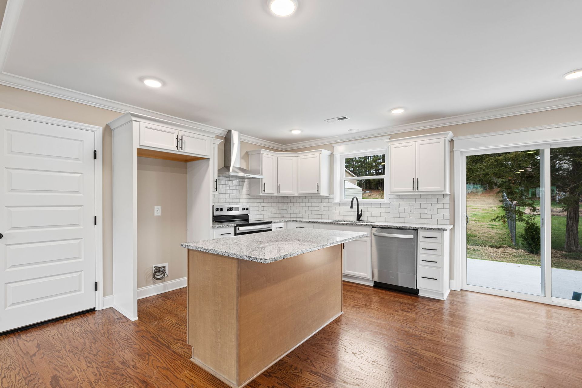 A kitchen with white cabinets , granite counter tops , stainless steel appliances and hardwood floors.