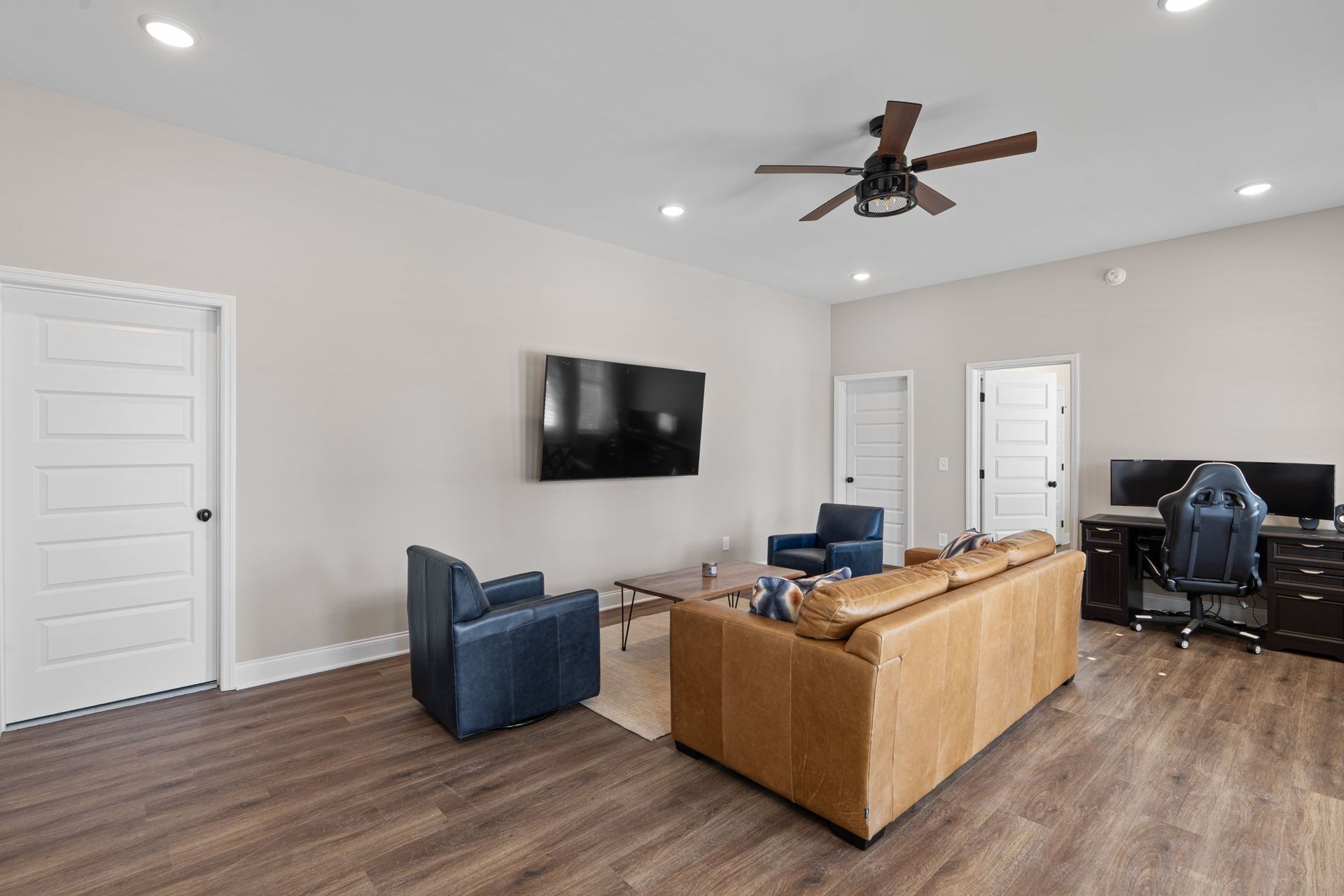 A living room with a couch , chairs , a television and a ceiling fan.