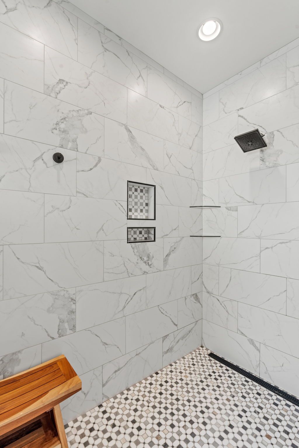 A walk in shower with marble tiles and a wooden bench.