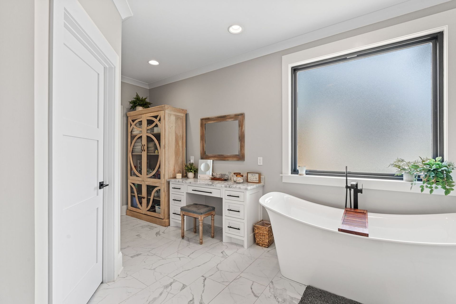 A bathroom with a tub , dresser , mirror and window.