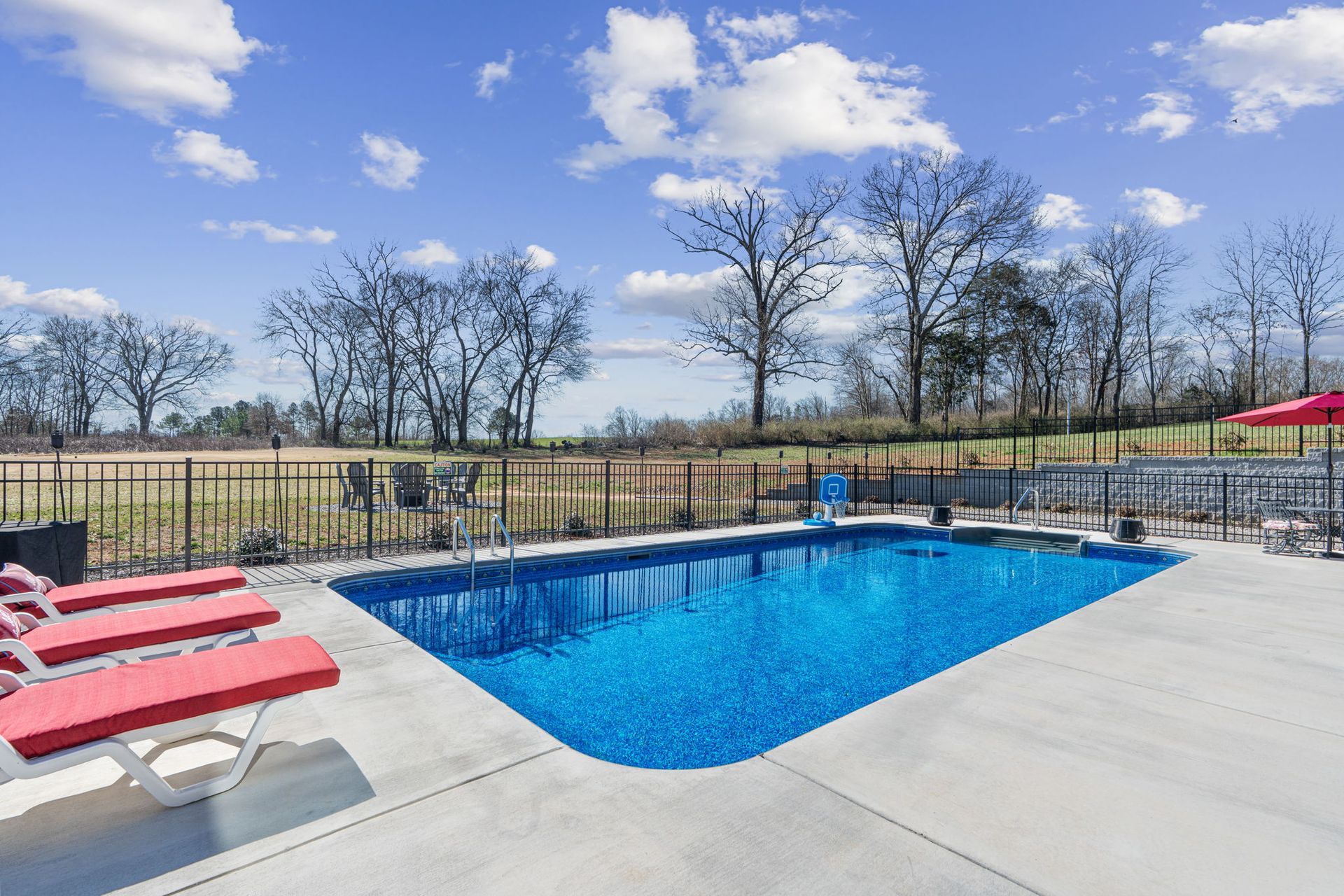 A large swimming pool surrounded by chairs and umbrellas on a sunny day.