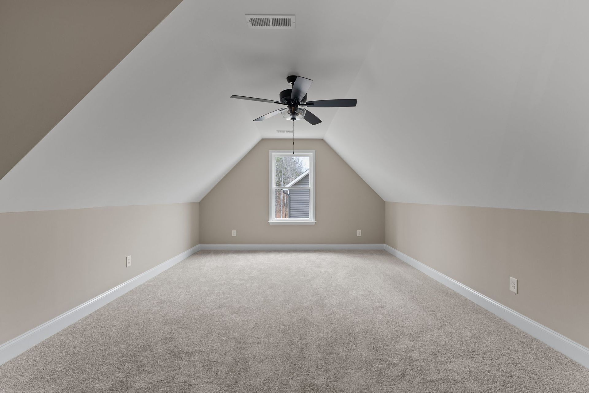 An empty attic with a ceiling fan and a window.