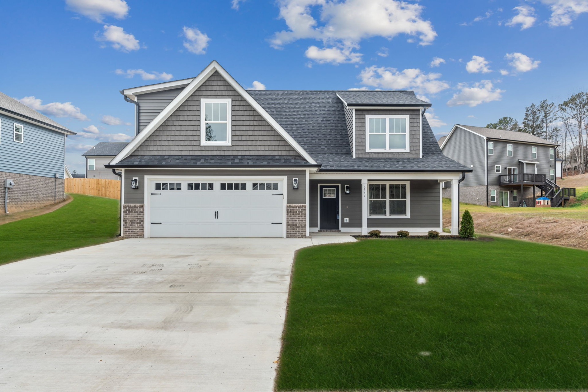 A large gray house with a white garage door is for sale.