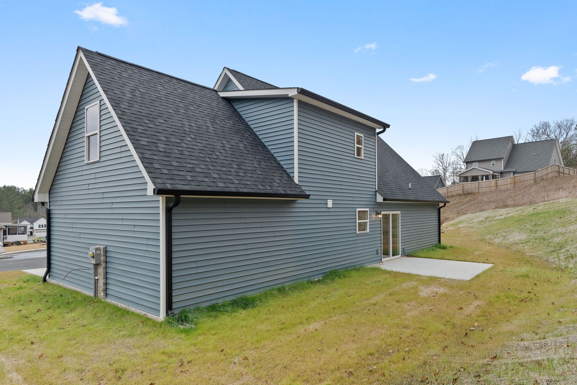 A gray house with a black roof is sitting on top of a grassy hill.