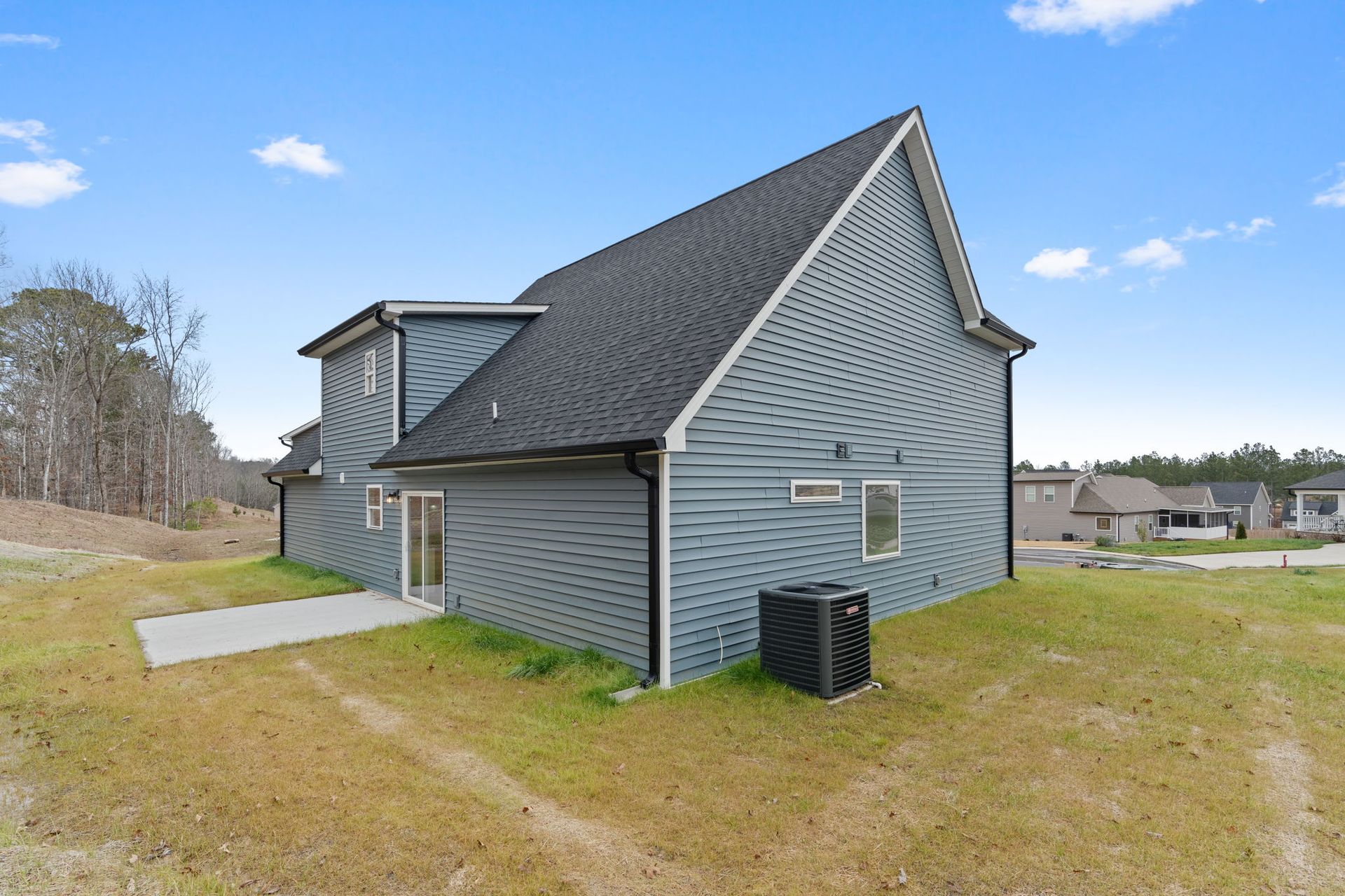 A house with a gray siding and a black roof is sitting on top of a lush green field.