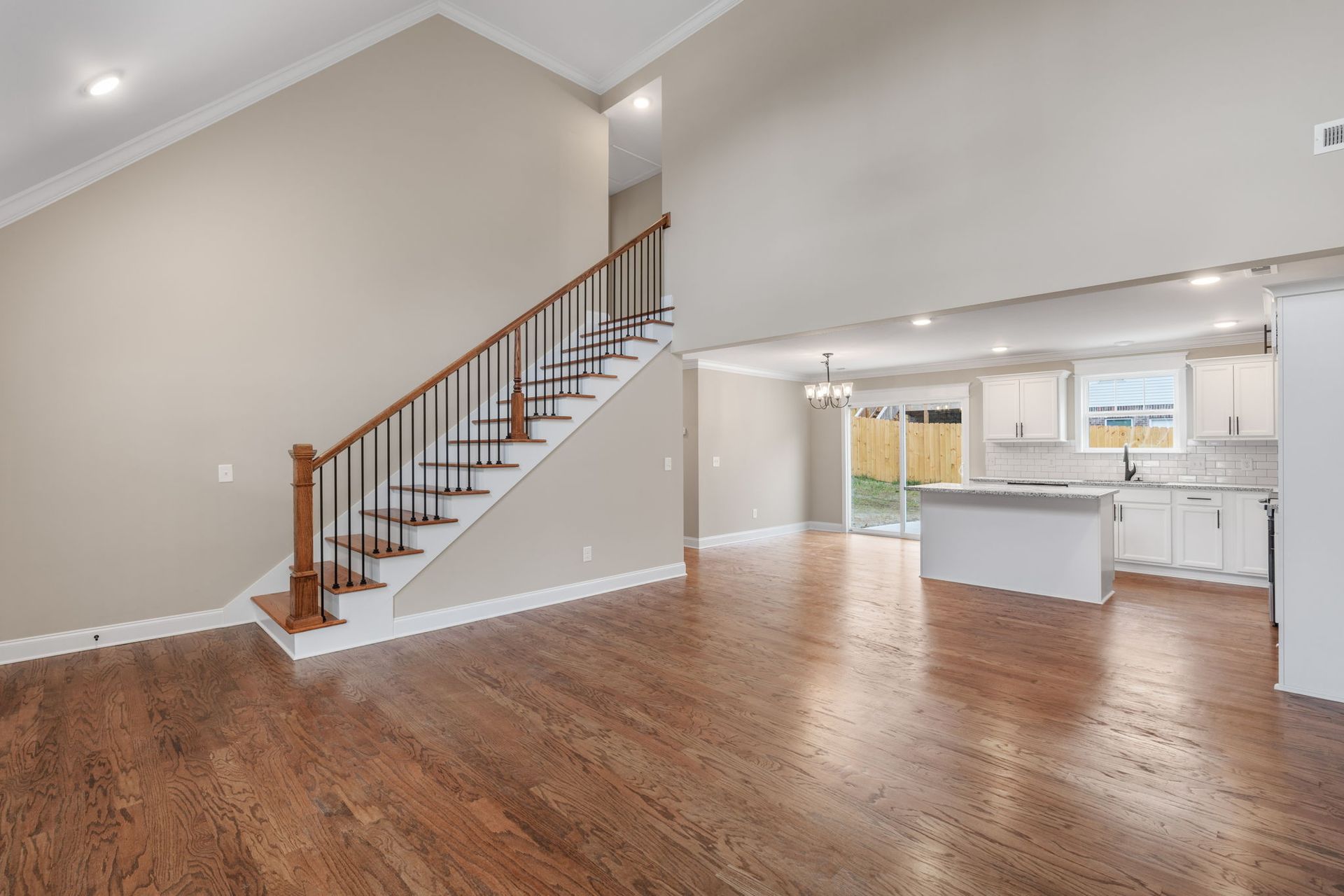An empty living room with hardwood floors and stairs leading up to the second floor.