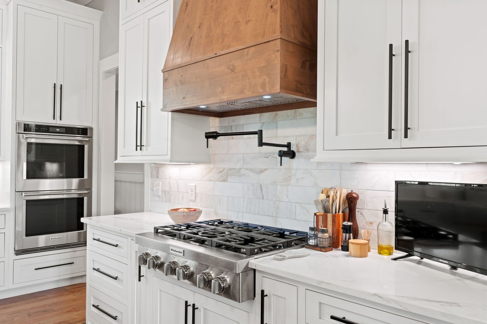 A kitchen with white cabinets , stainless steel appliances and a wooden hood.
