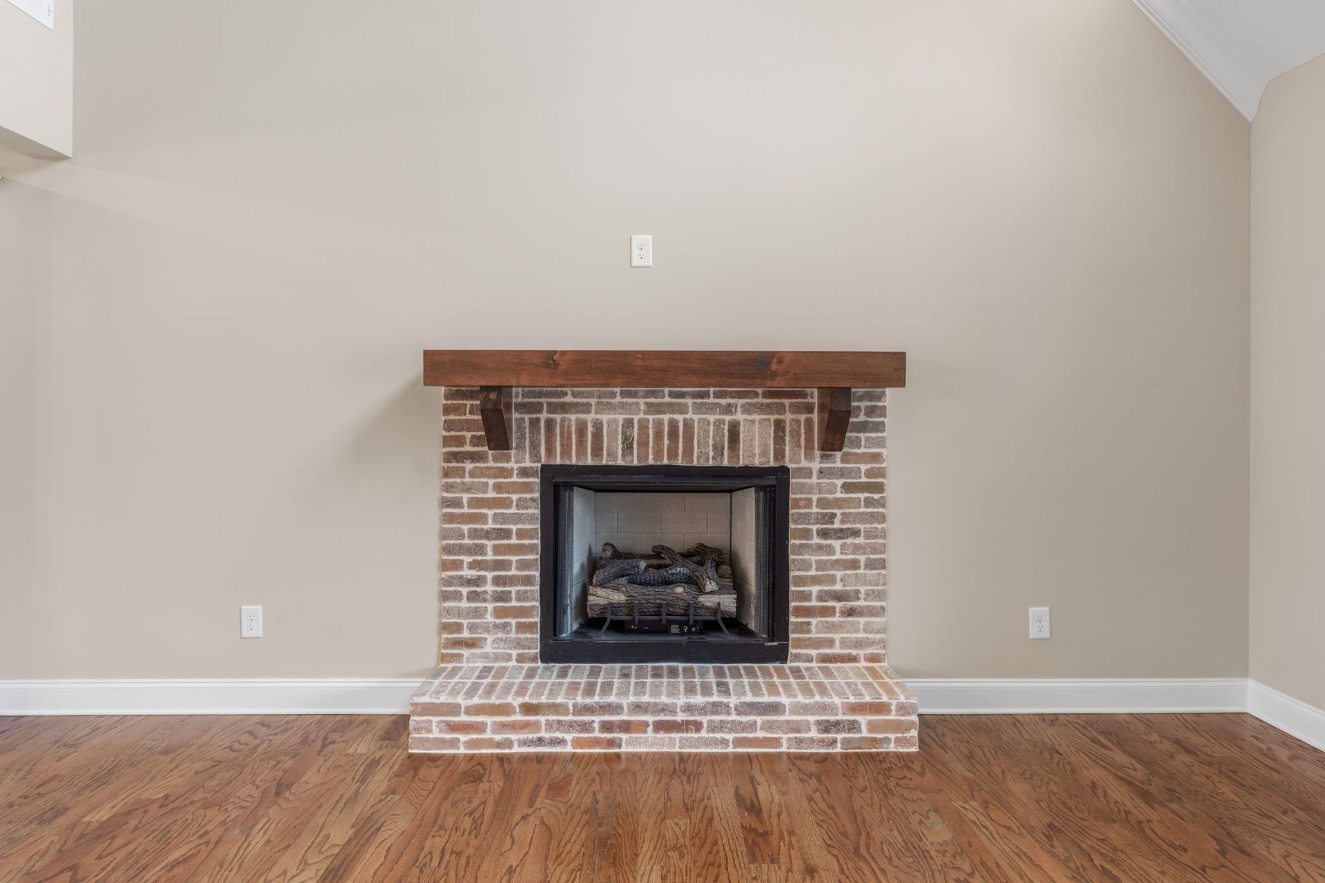 An empty living room with a brick fireplace and hardwood floors.