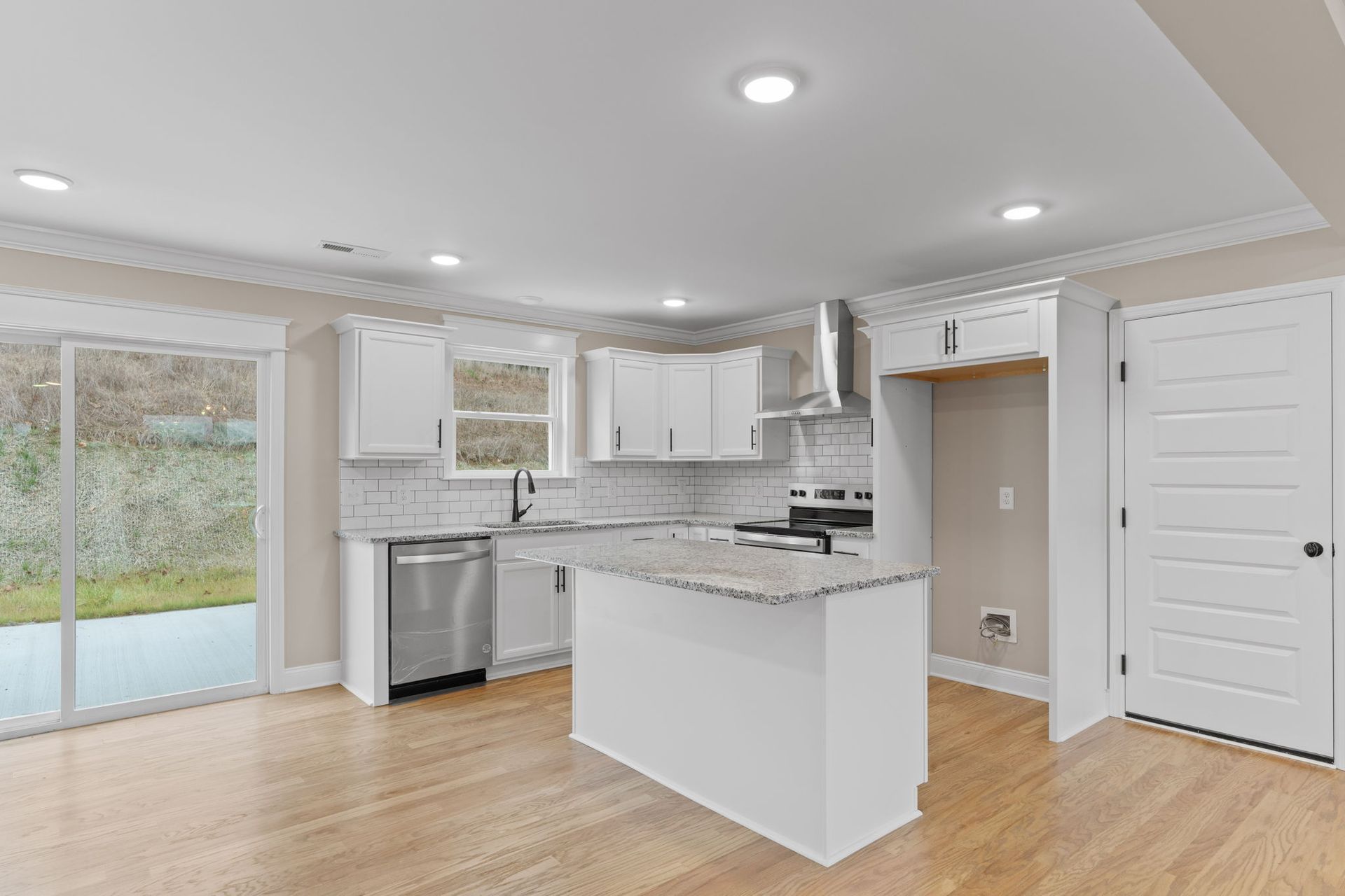 An empty kitchen with white cabinets , granite counter tops , stainless steel appliances , and hardwood floors.
