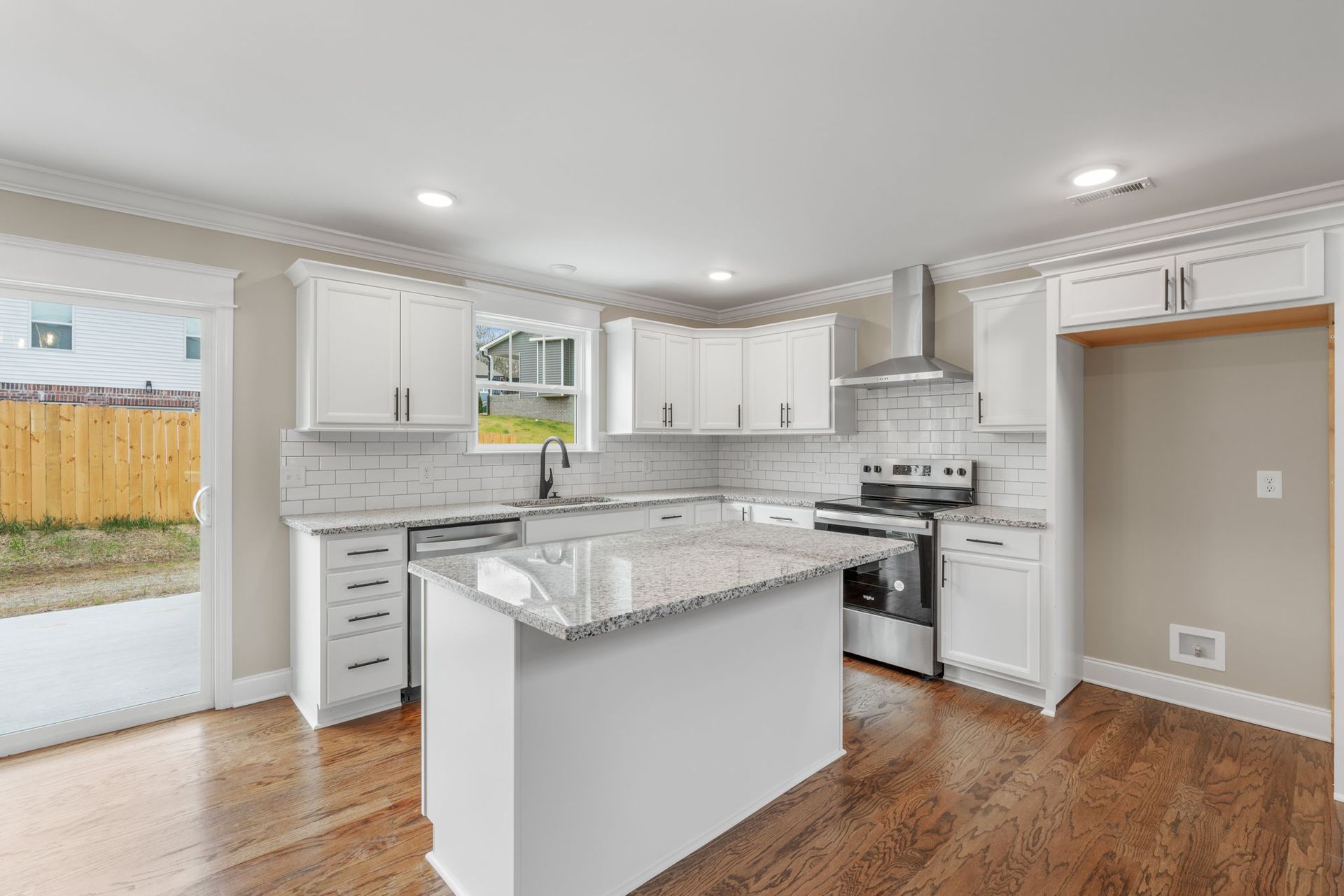 A kitchen with white cabinets , granite counter tops , stainless steel appliances and hardwood floors.
