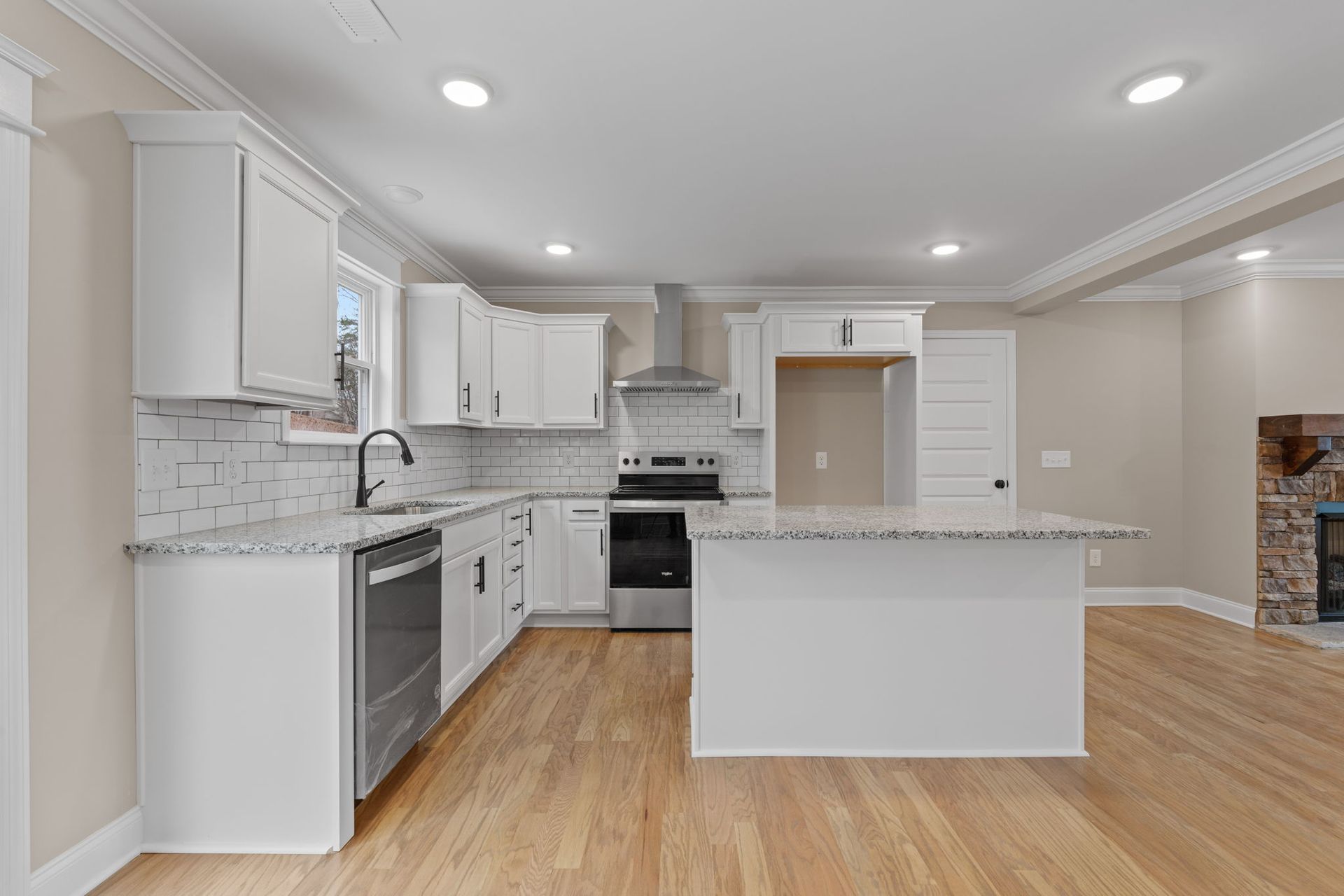 A kitchen with white cabinets , stainless steel appliances , granite counter tops and hardwood floors.