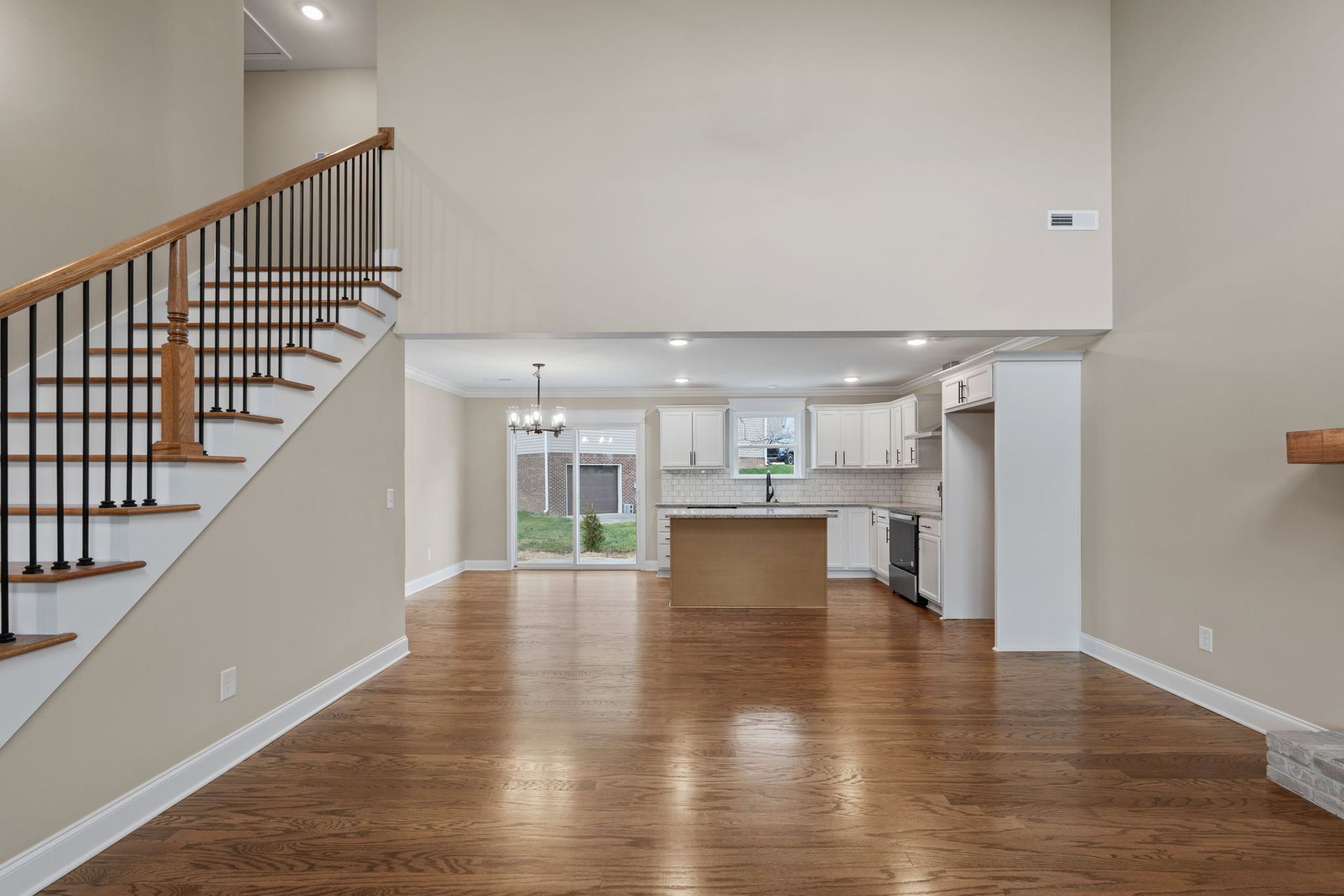 An empty living room with hardwood floors and stairs leading to a kitchen.
