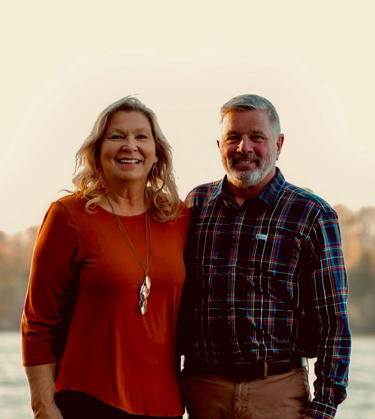 A man and a woman are posing for a picture in front of a body of water.